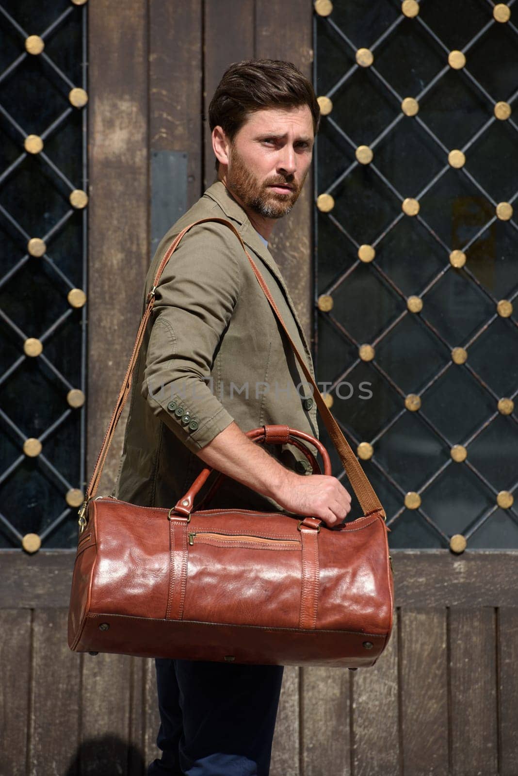 a man with a bag. black leather travel bag, street photo. man is wearing blue sneakers, jeans, a white T-shirt and a jacket by Ashtray25