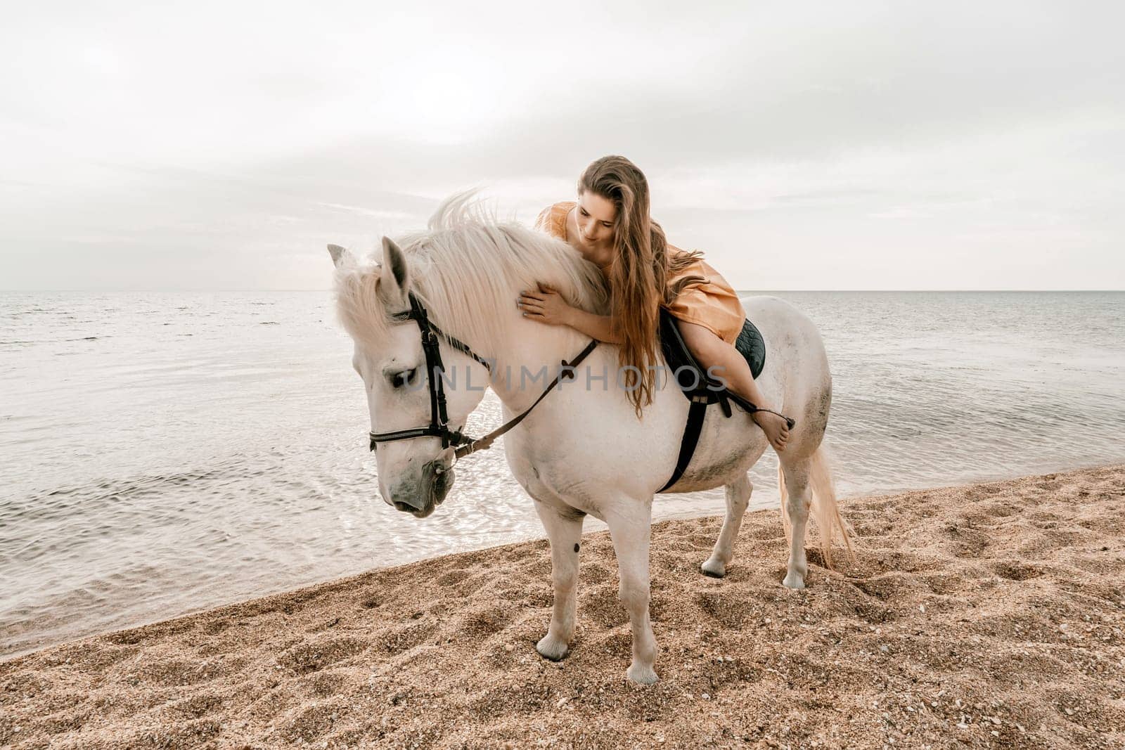 A white horse and a woman in a dress stand on a beach, with the sky and sea creating a picturesque backdrop for the scene