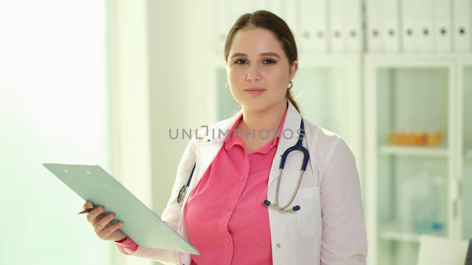 Portrait of happy confident female doctor posing with clipboard and looking at camera by kuprevich