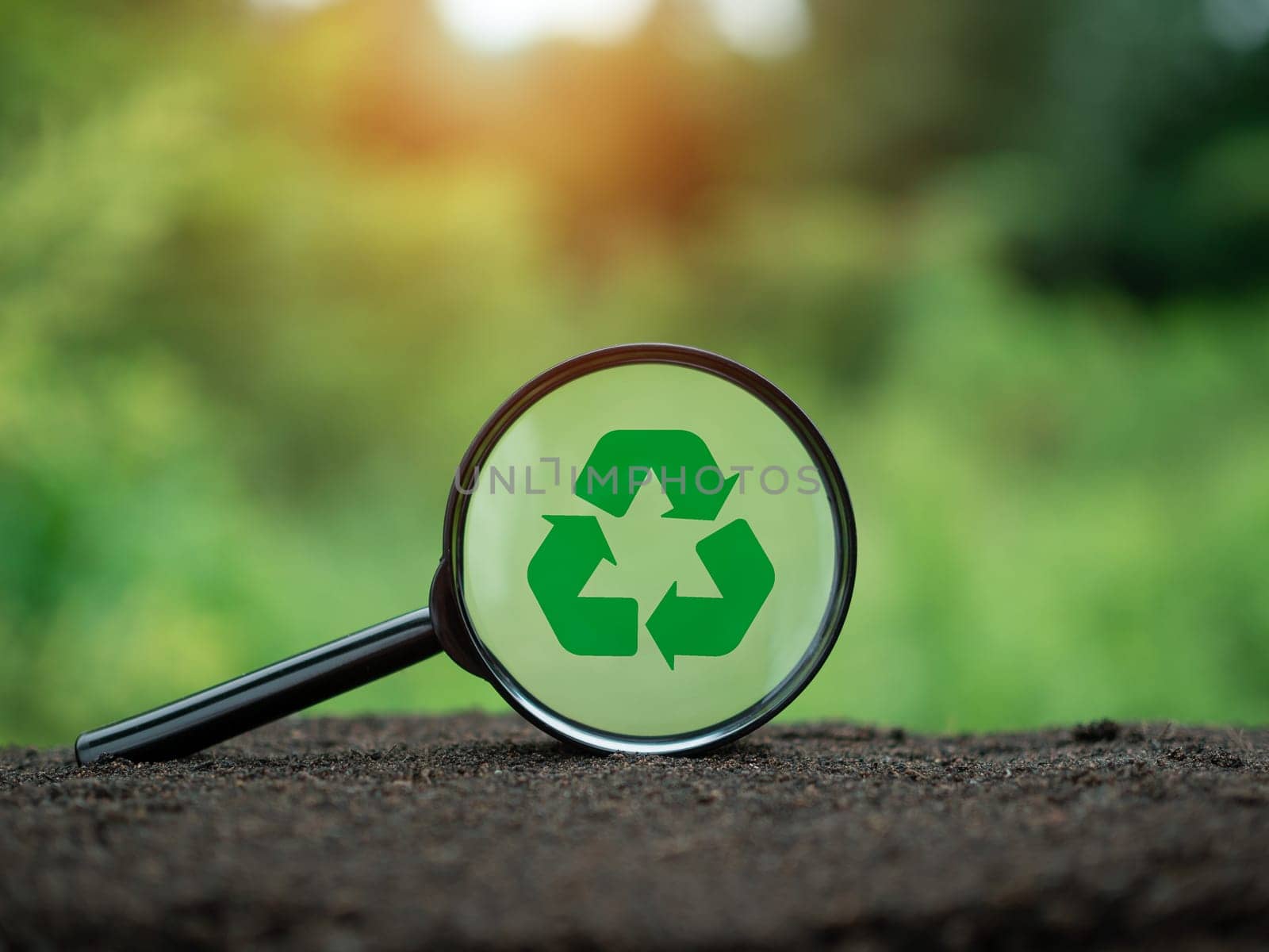 Concepts of waste reduction, pollution, reuse, efficient use of resources. Recycling symbol in magnifying glass on nature background.