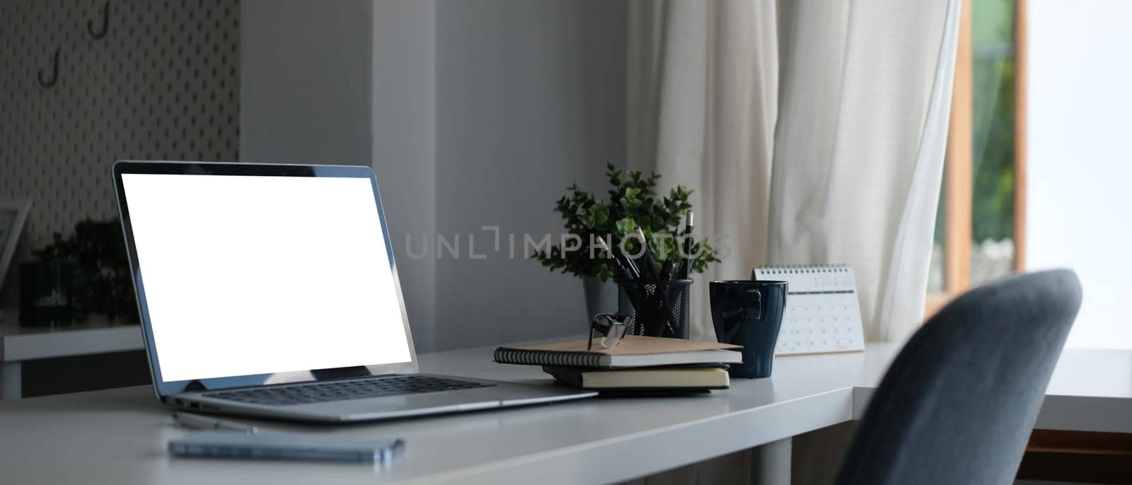 Laptop with blank display, coffee cup and stationery on white office desk.
