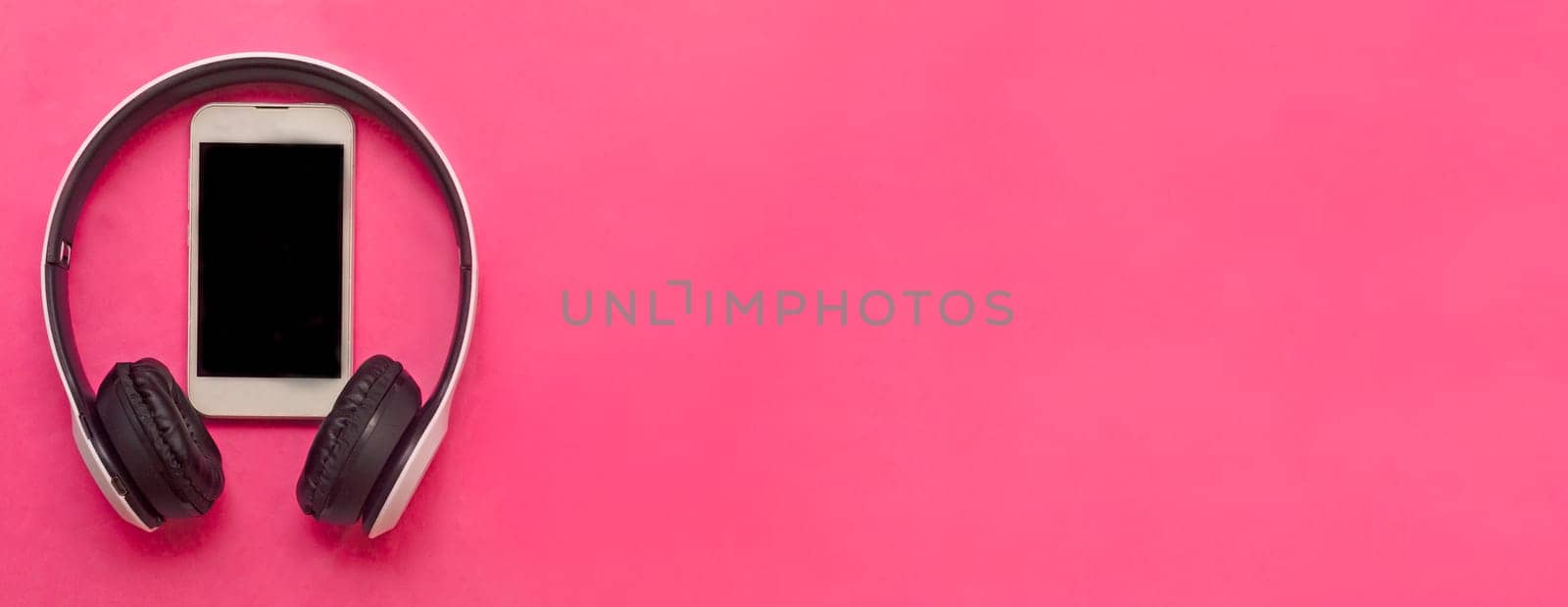 White wireless headphones and white smartphone on pink background.Listening of modern music in travel.