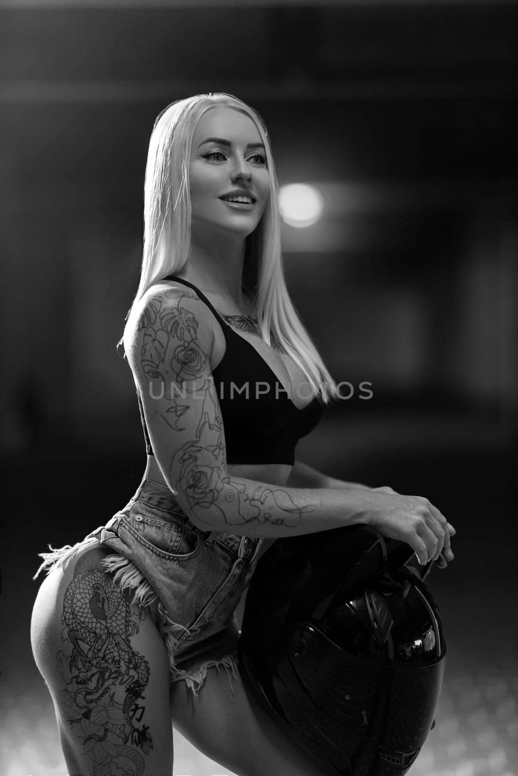 Blonde girl with a motorcycle helmet posing in a covered parking lot by but_photo