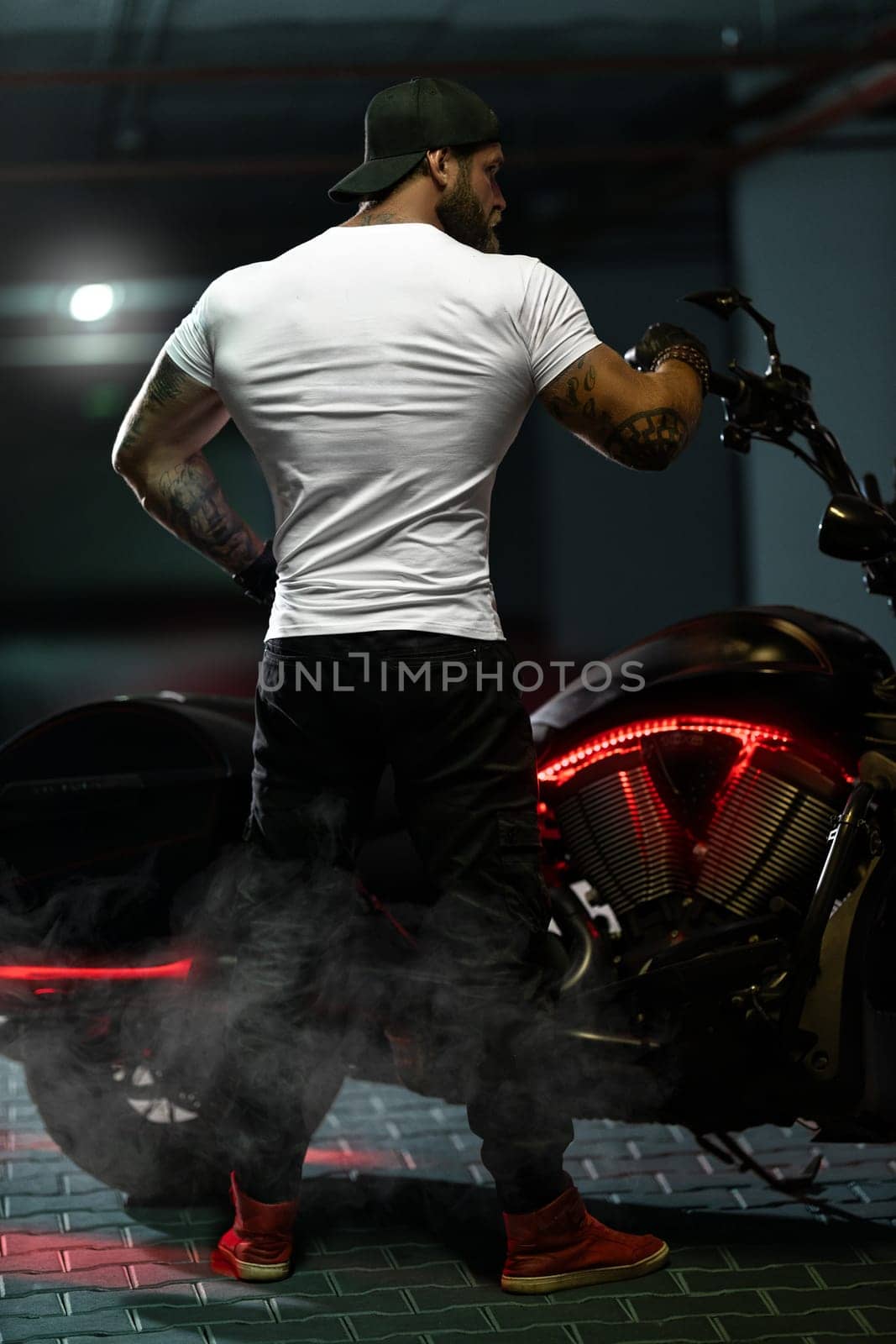 Athletic bearded biker man posing with motorbike with his back to the frame by but_photo
