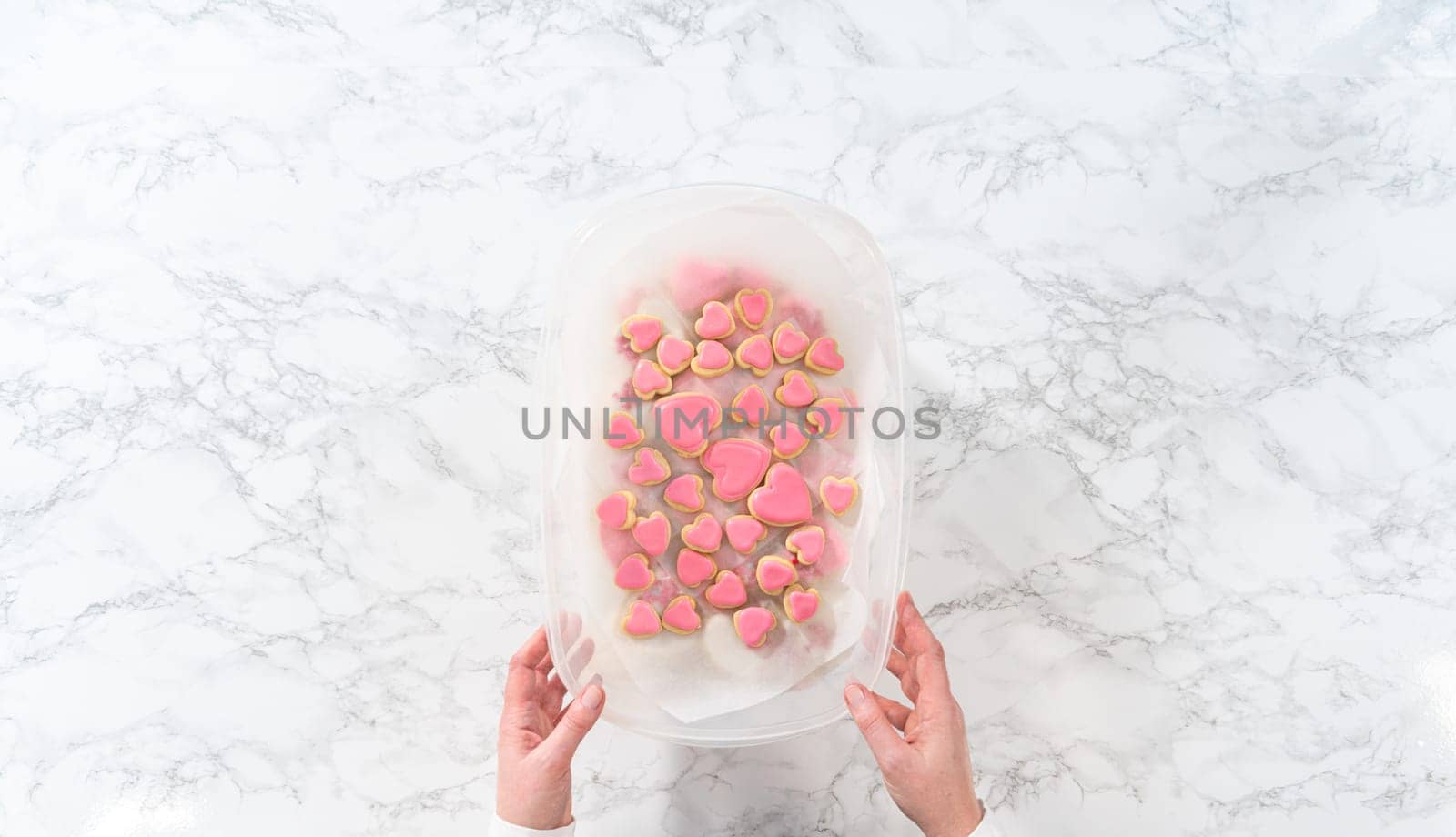 Flat lay. Storing heart-shaped sugar cookies with pink and white royal icing in a large plastic container.
