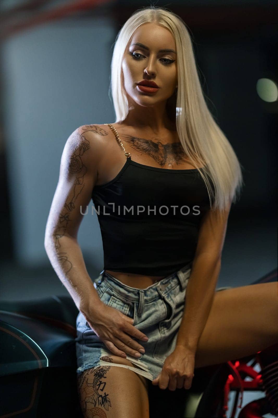 Sexy blonde girl with tattoos posing leaning on motorcycle in the parking by but_photo