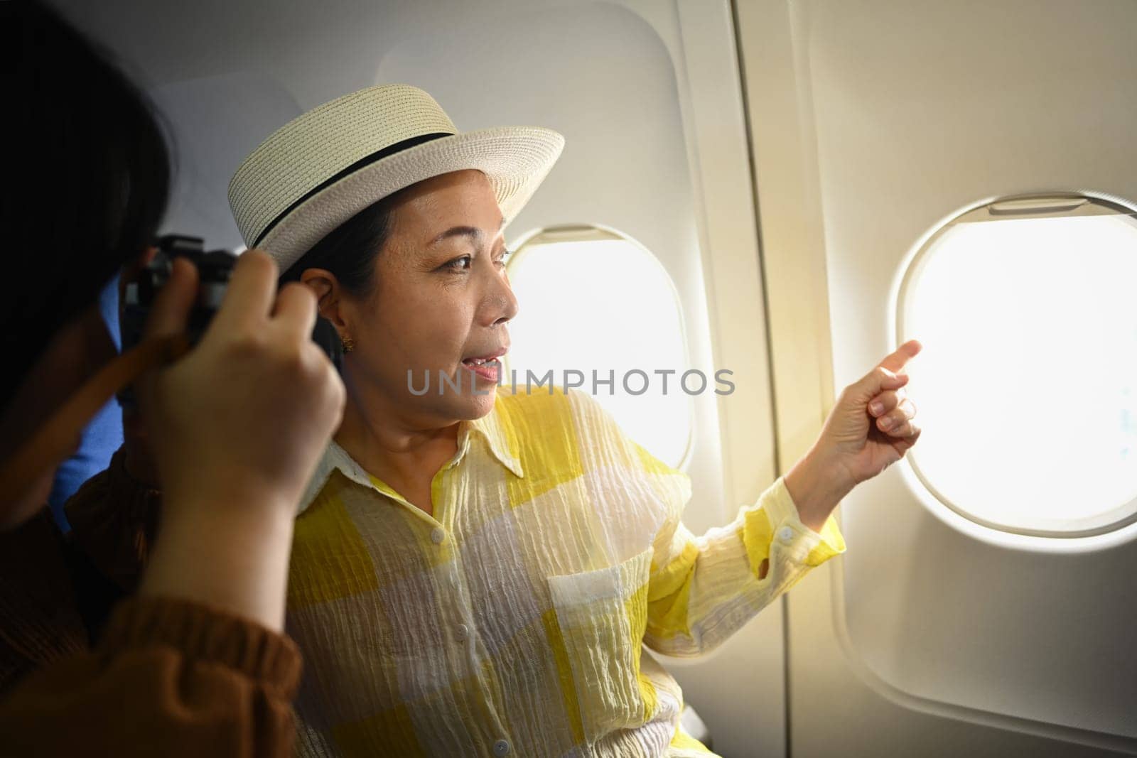 Smiling middle aged woman and daughter sitting in passenger airplane and taking picture, waiting for airplane landing by prathanchorruangsak