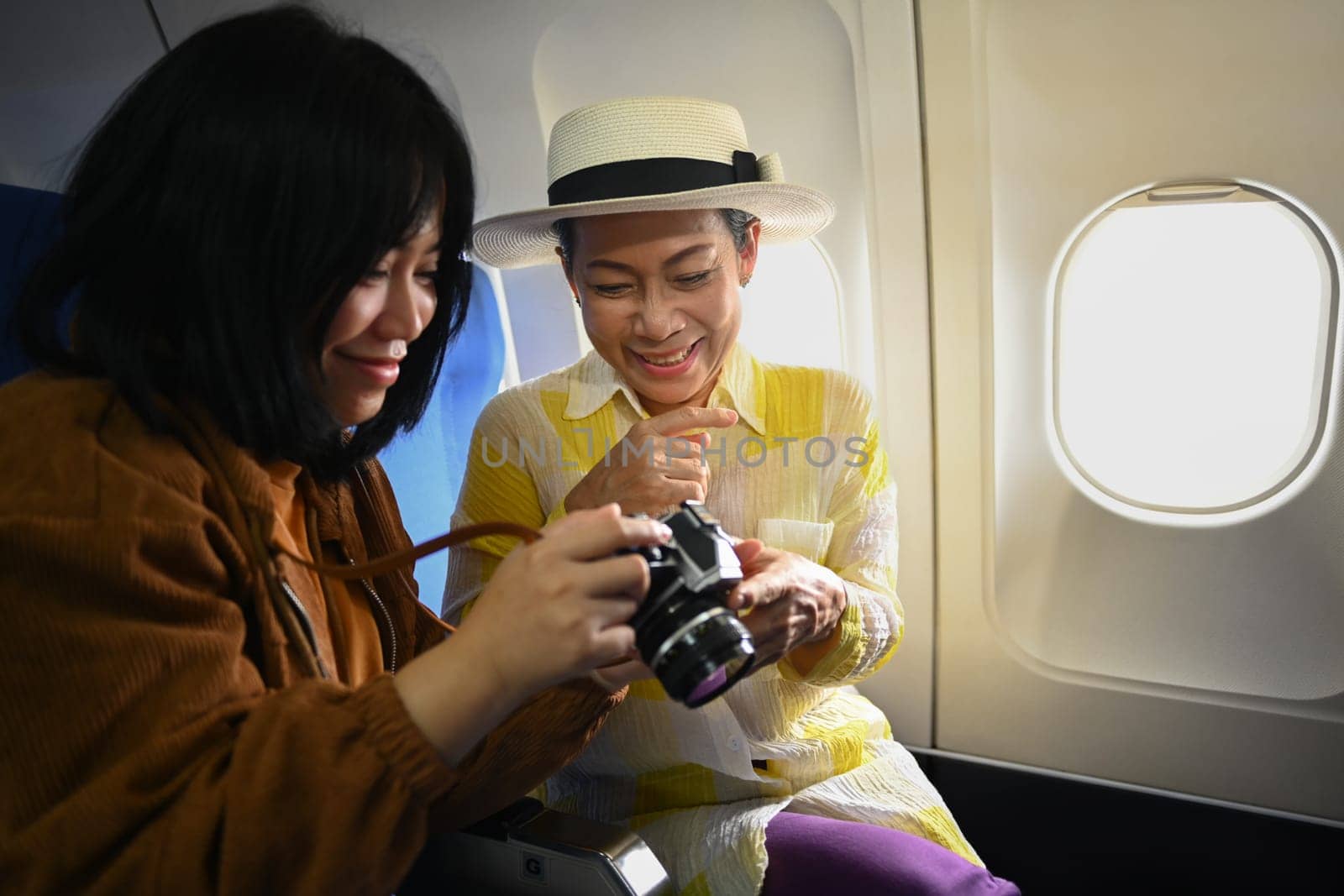 Smiling middle aged woman and daughter sitting in passenger airplane and taking picture, waiting for airplane landing.