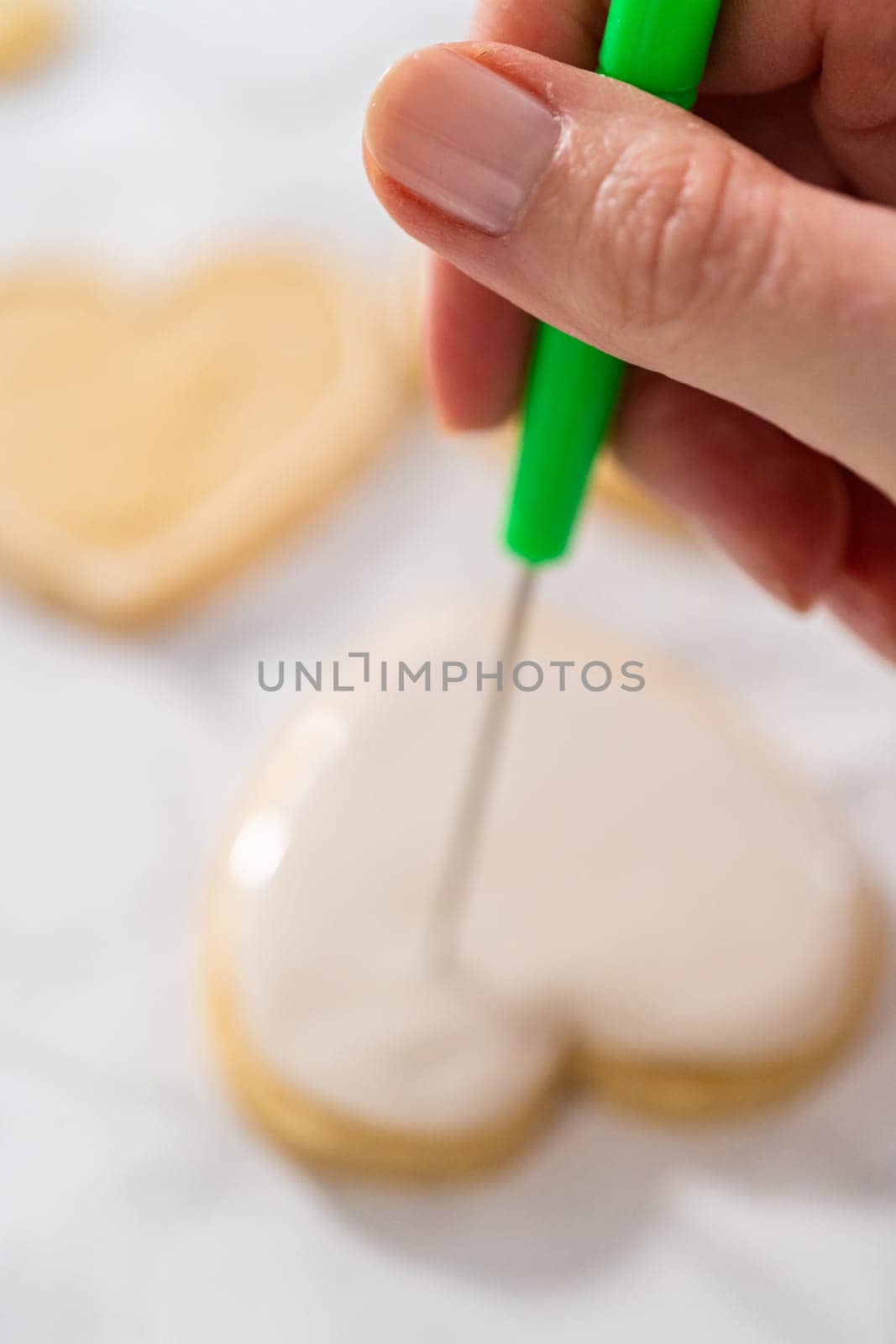 Decorating heart-shaped sugar cookies with pink and white royal icing for Valentine's Day.