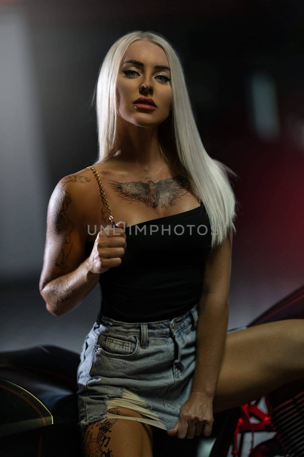 Sexy blonde girl with tattoos posing leaning on motorcycle in the parking by but_photo