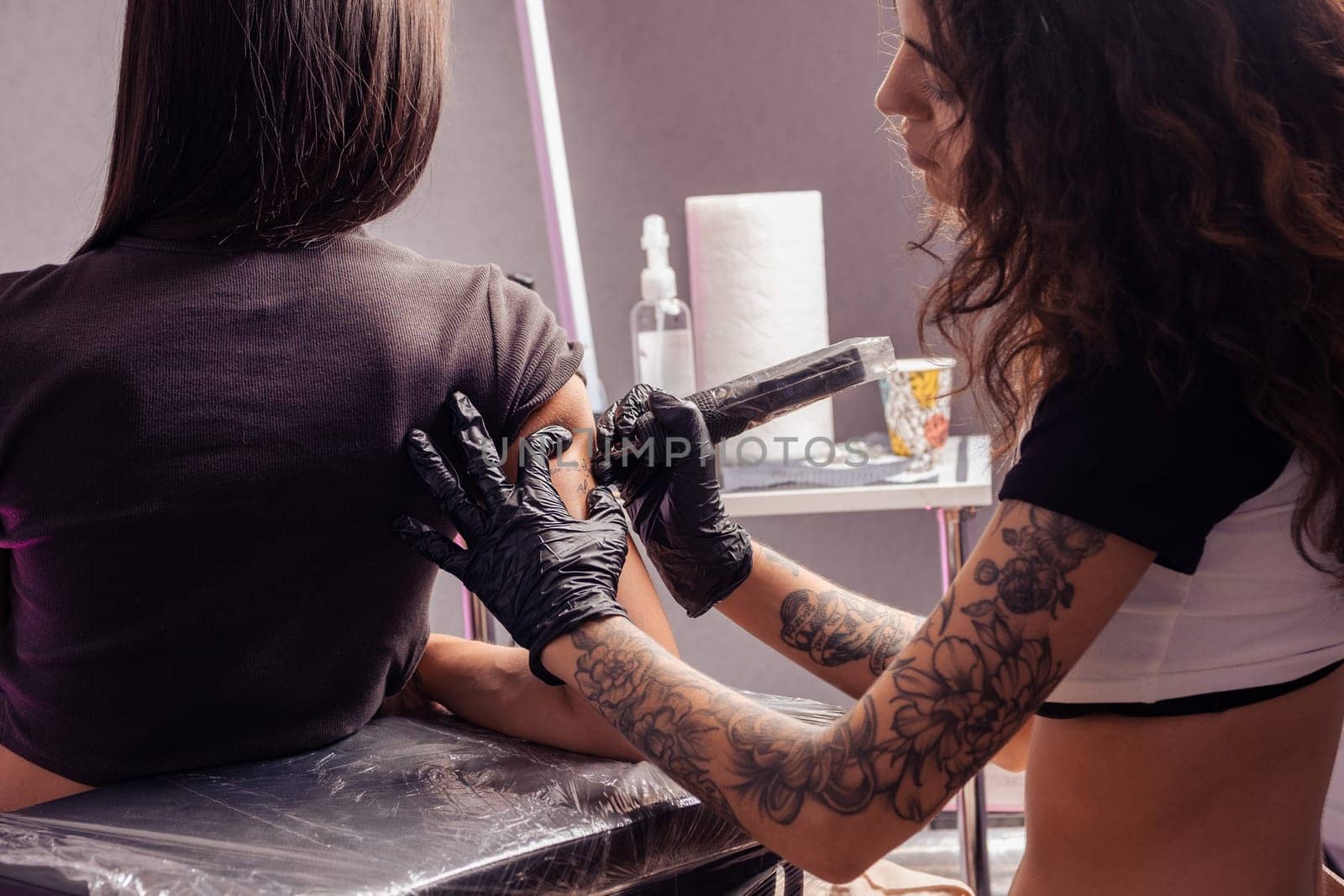 Focused girl tattooist creating tattoo with lettering on arm of woman by nazarovsergey
