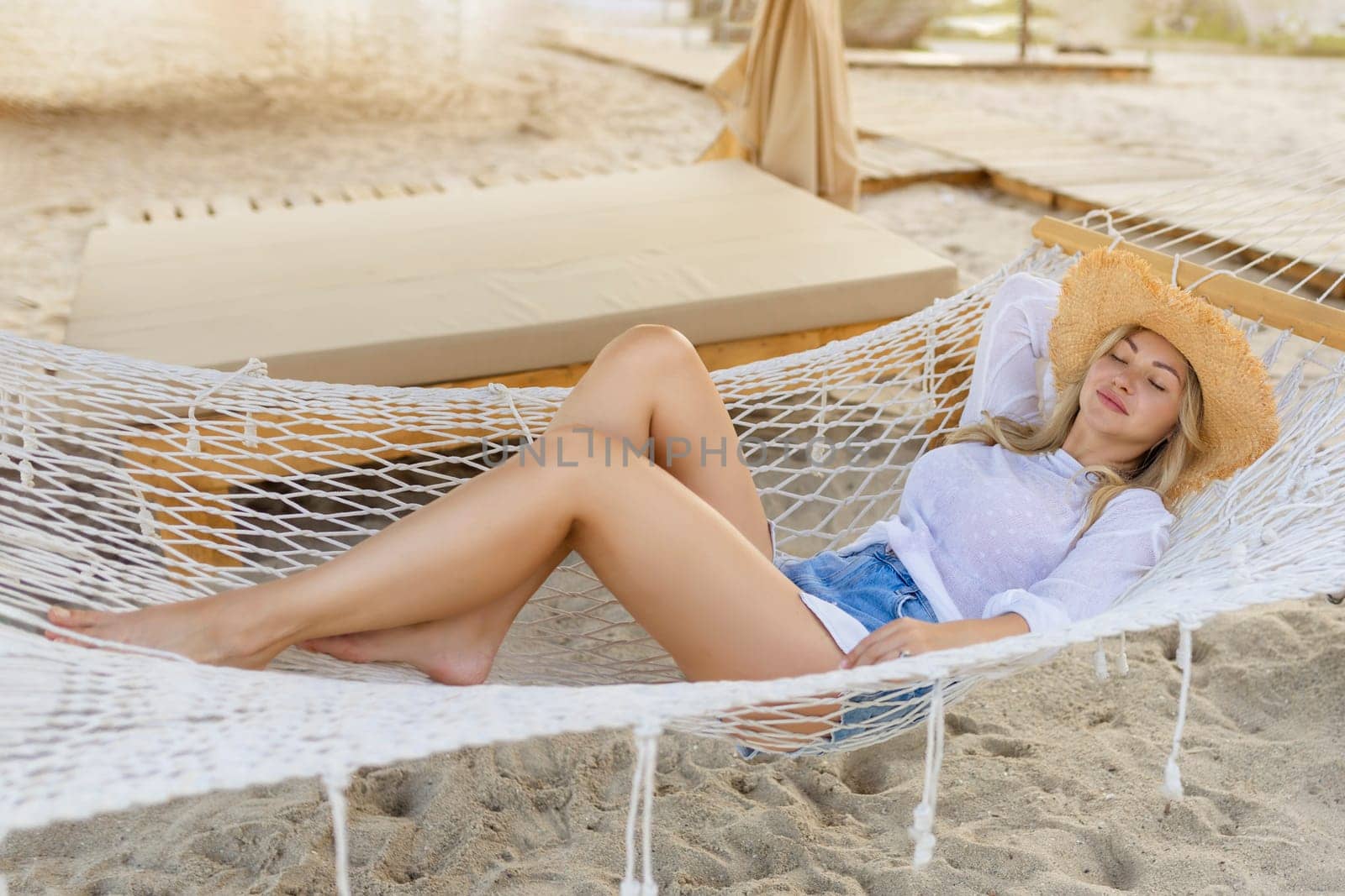 Happy female traveler relaxing in a hammock on a paradise beach. Woman tourist in a straw hat near the tropical sea. vacation, travel, summer, wanderlust and holiday concept.