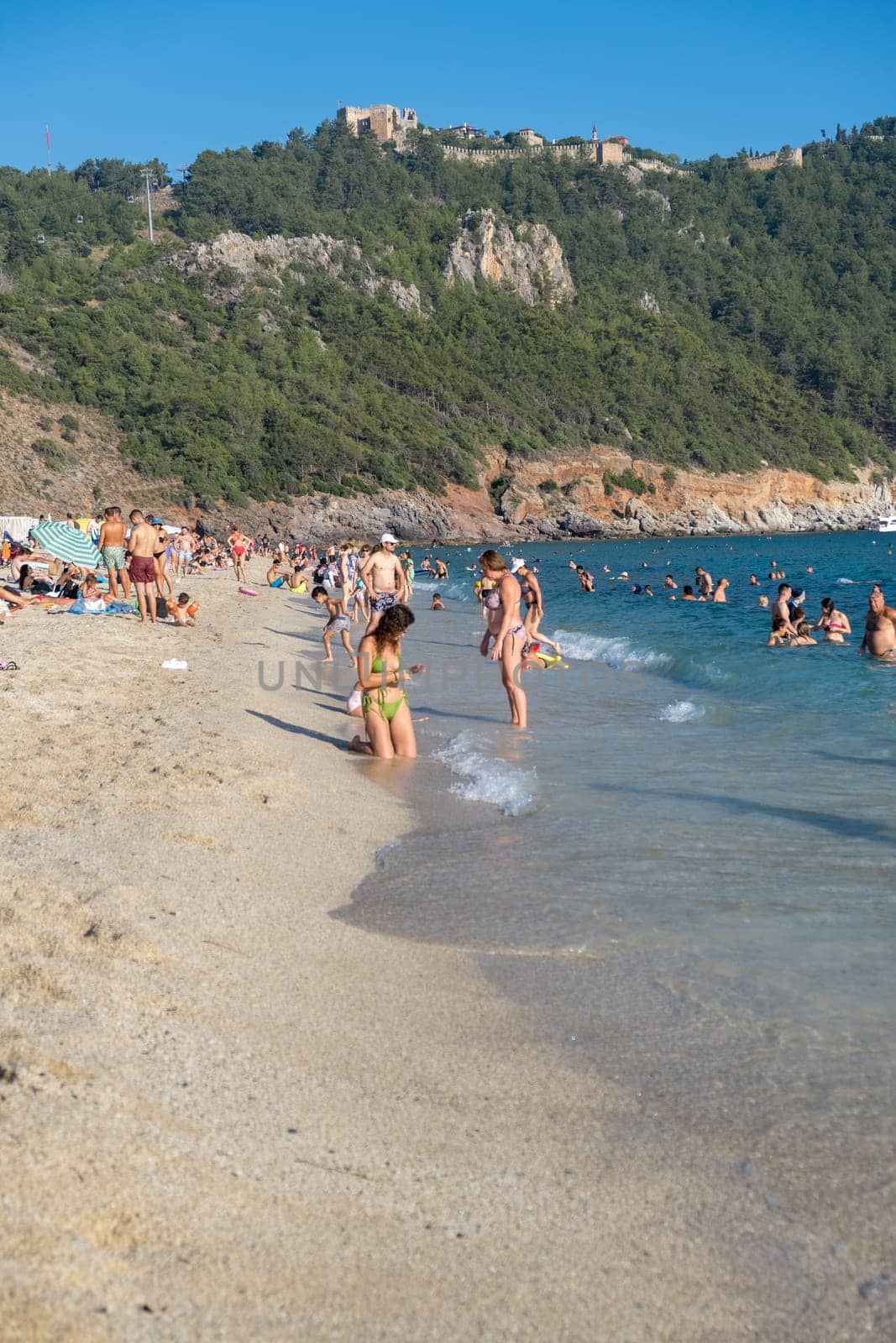 Alanya, Turkey, 02. 07. 2021. People Crowd Relaxing On Beach. Swimming people in sea. The best beach in Turkey with turquoise waters, Mediterranean Sea