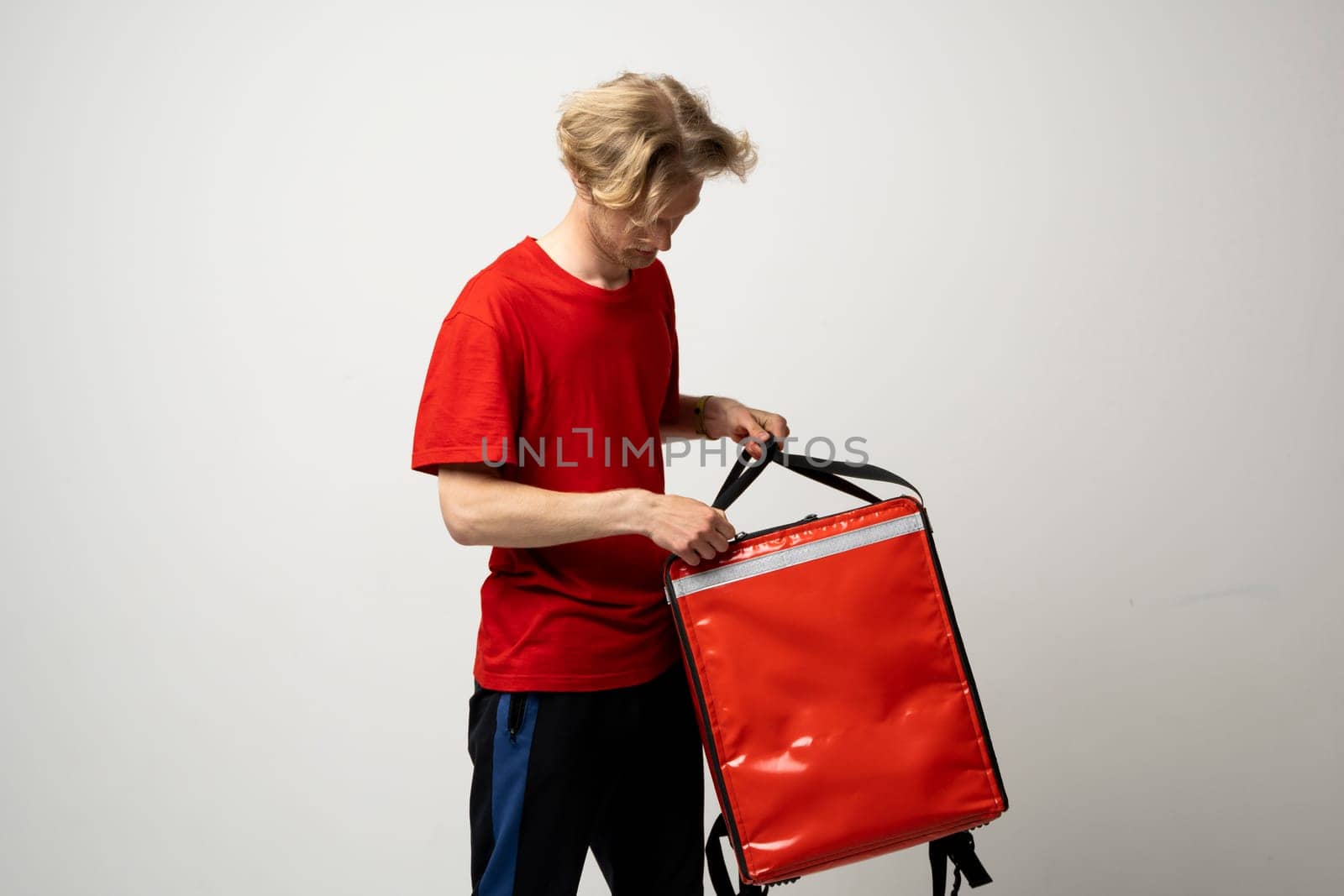 Delivery employee man guy male 20s in red uniform with thermal food bag backpack. Working in a courier service. Food delivery service. by vovsht