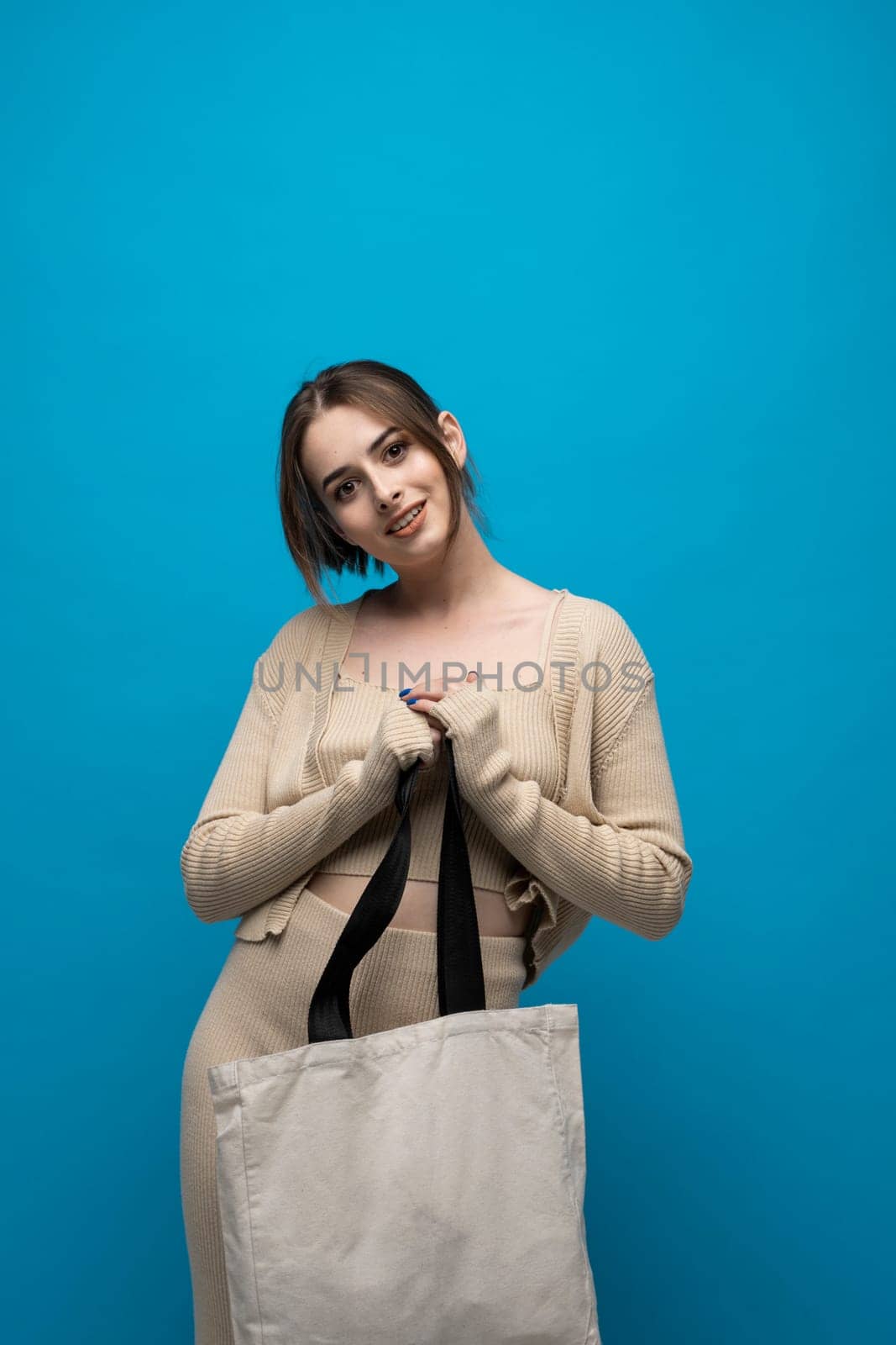 Brunette cheerful millennial woman holding white eco bag standing over white studio background. Lady holding flax shopper handbag. Fashion and ecology concept. by vovsht