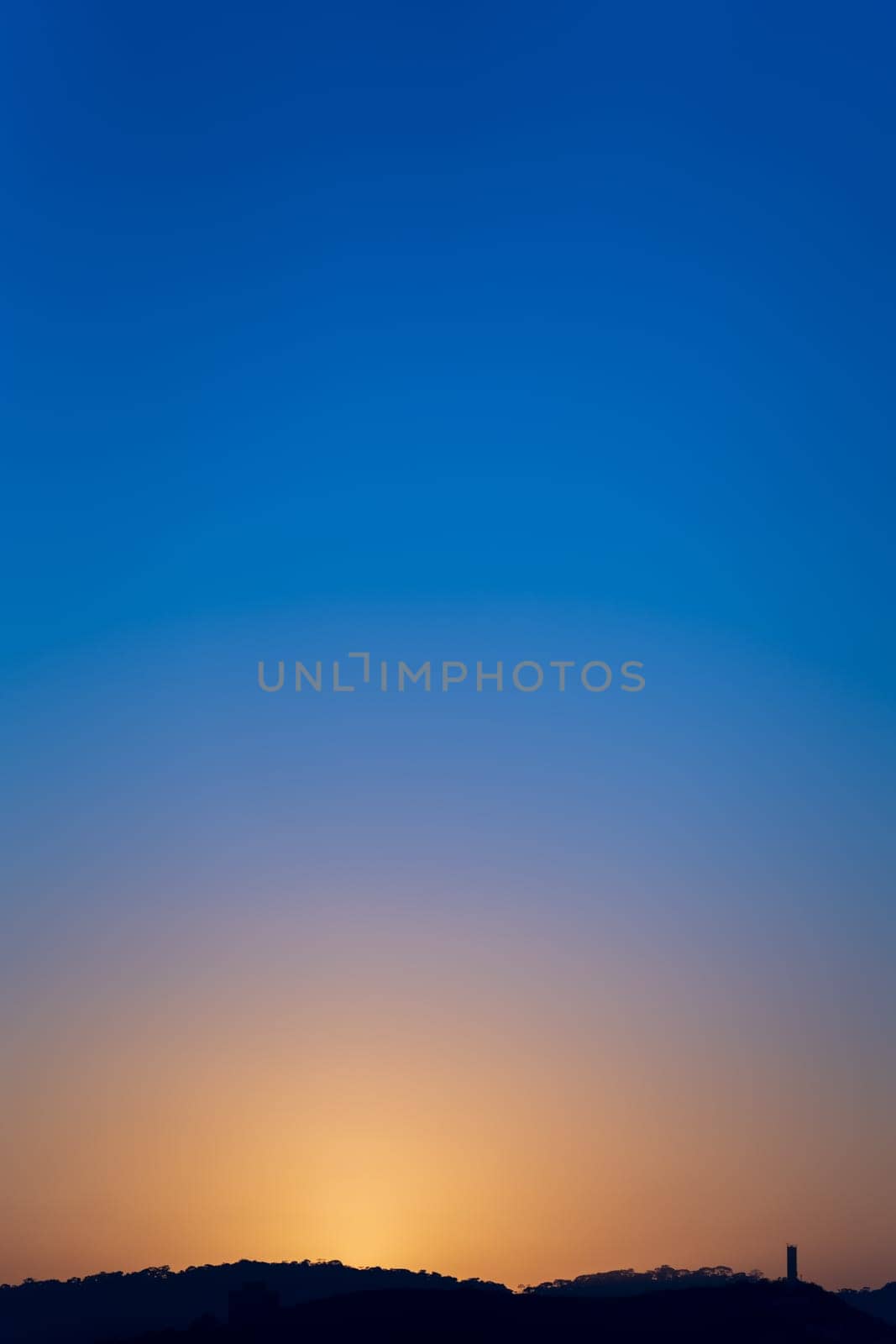 Sunrise behind a mountain and tower, with the blue sky transitioning to warm sunlight hues.