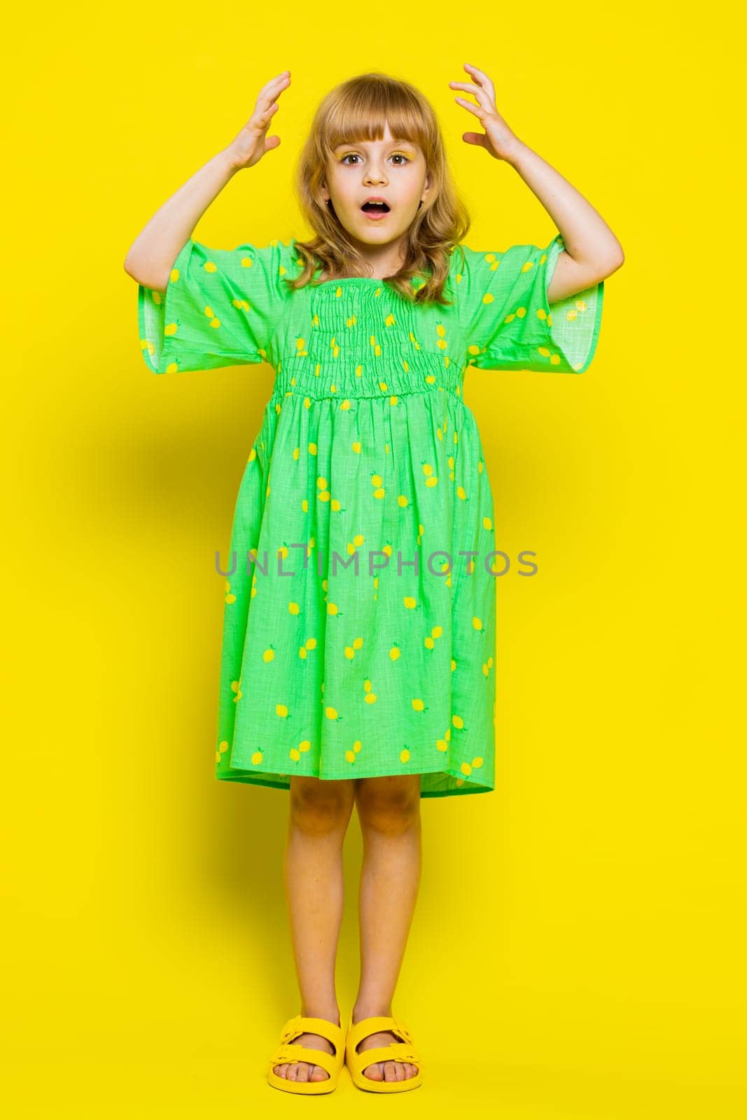 Excited amazed child girl kid looking shocked surprised wow showing hands brain head explosion gesture. Little preteen children touching her head and showing explosion on yellow background. Vertical