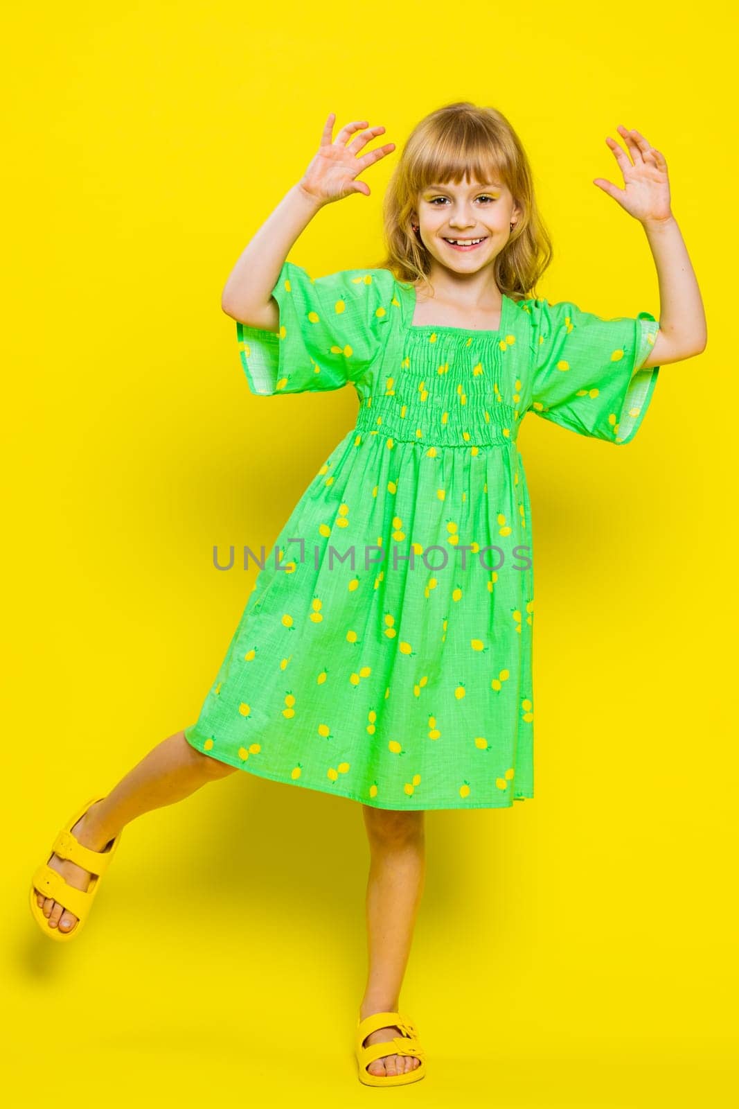 Young blonde child girl kid listening music dancing disco fooling around having fun expressive gesticulating hands, relaxing on party. Little preteen children isolated on yellow background. Vertical