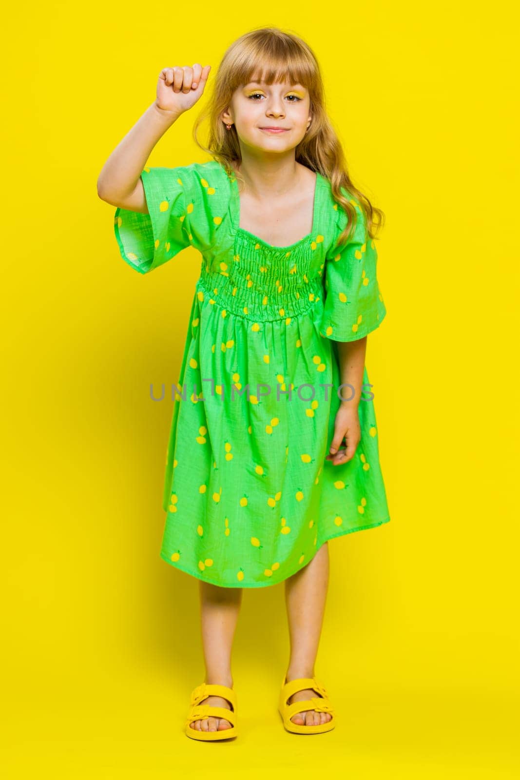 Knock-knock who is there. Confused young blonde child girl kid knocking door gesture asking who is at home, feeling embarrassed, no idea, being clueless uncertain. Little preteen children. Vertical