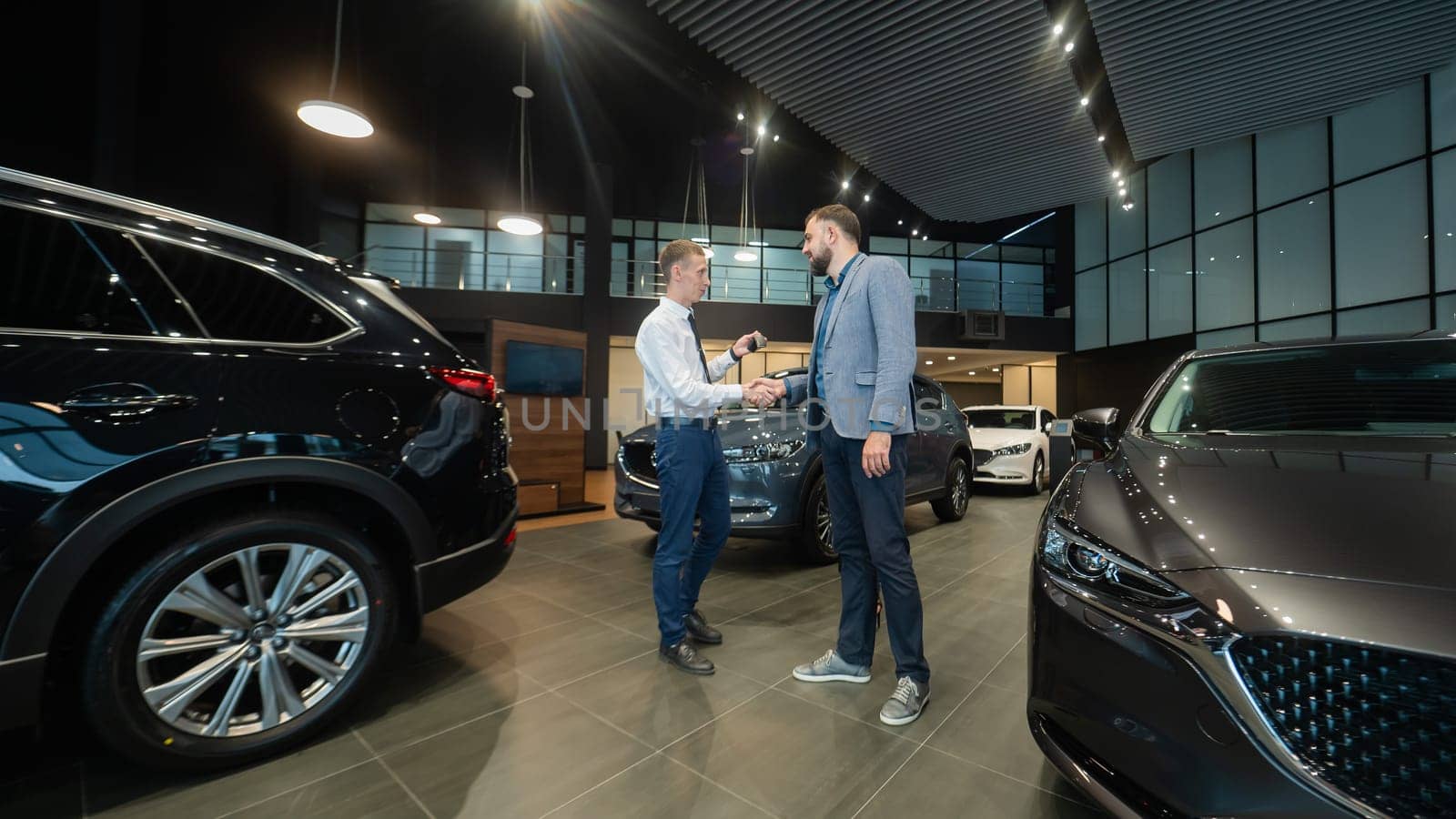 Caucasian man shakes hands with a salesman in a car dealership. Car purchase deal. by mrwed54
