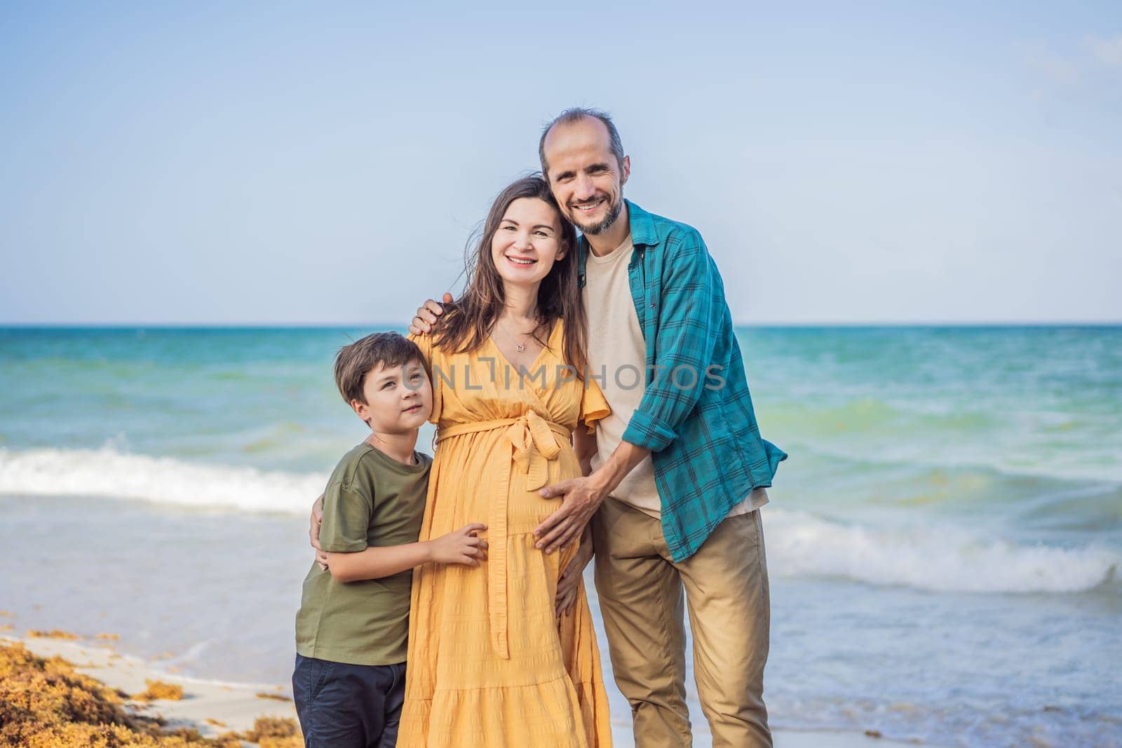 A loving family enjoying tropical beach - a radiant pregnant woman after 40, embraced by her husband, and accompanied by their adult teenage son, savoring precious moments together amidst nature's beauty. Pregnancy after 40 concept by galitskaya
