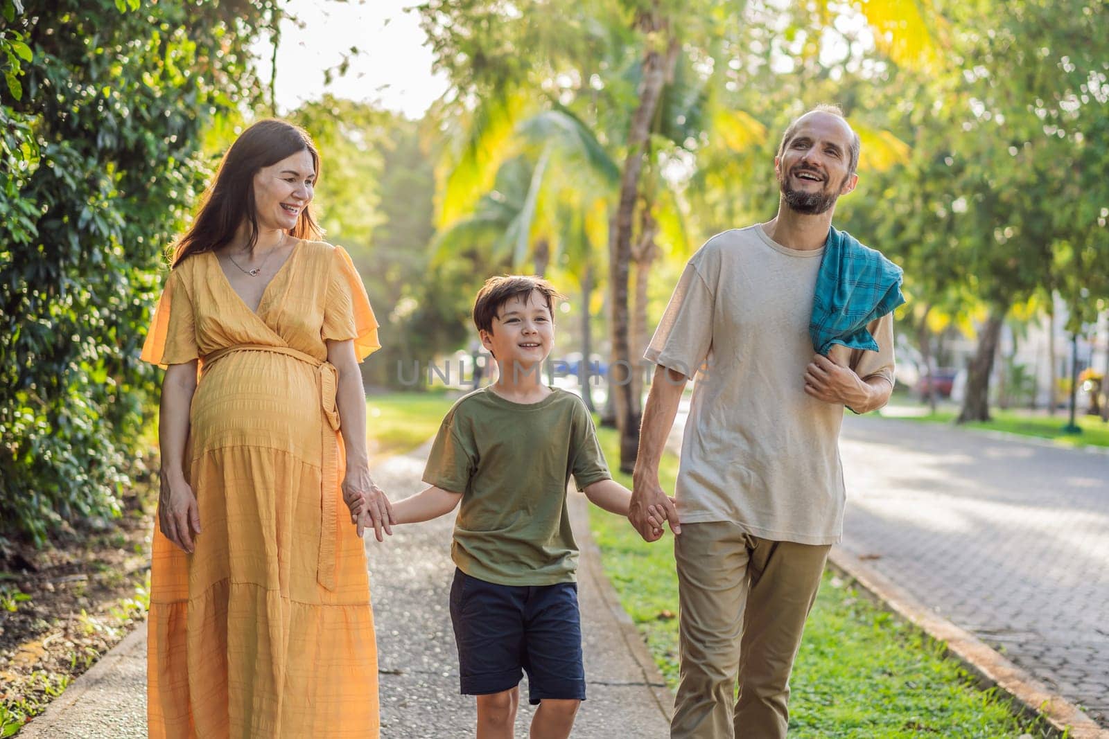 A loving family enjoying a leisurely walk in the park - a radiant pregnant woman after 40, embraced by her husband, and accompanied by their adult teenage son, savoring precious moments together amidst nature's beauty. Pregnancy after 40 concept.