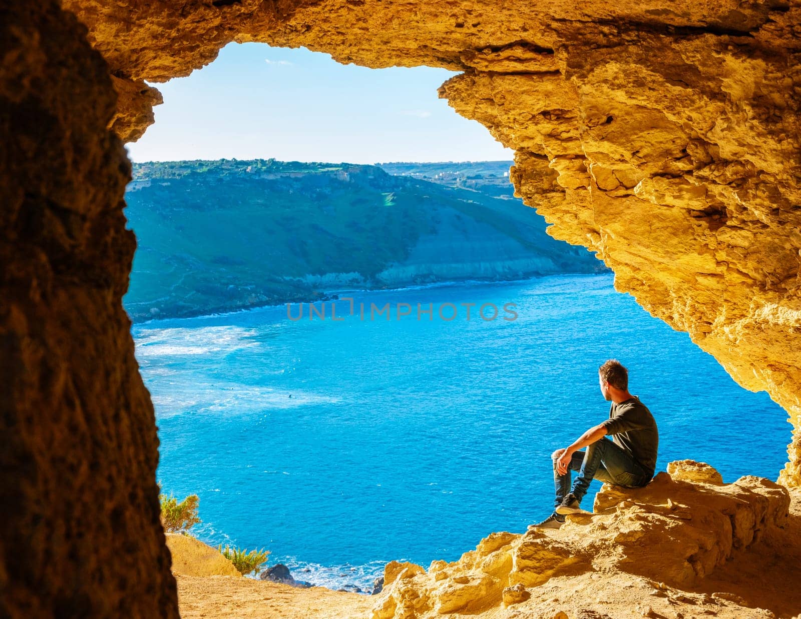 Gozo Island Malta, a young men and a View of Ramla Bay, from inside Tal Mixta Cave Gozo looking out over the blue ocean on a bright day during winter in Malta