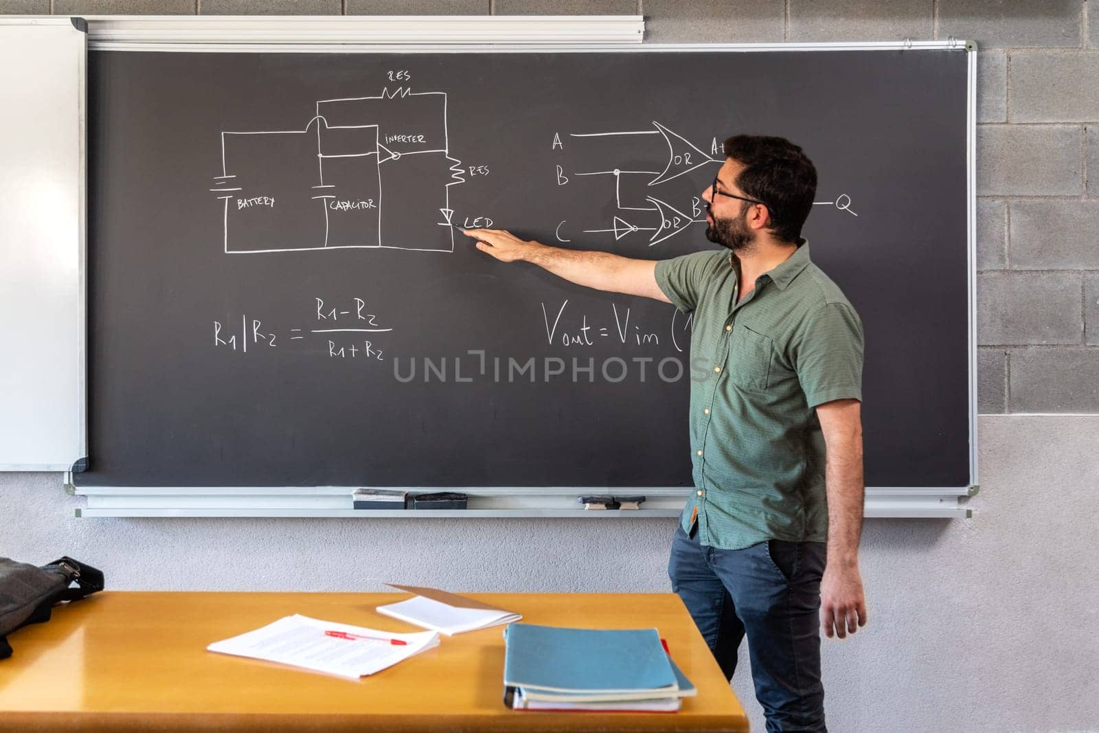 Teacher in classroom explaining concepts using blackboard. Online professor teaching via online call. by Hoverstock