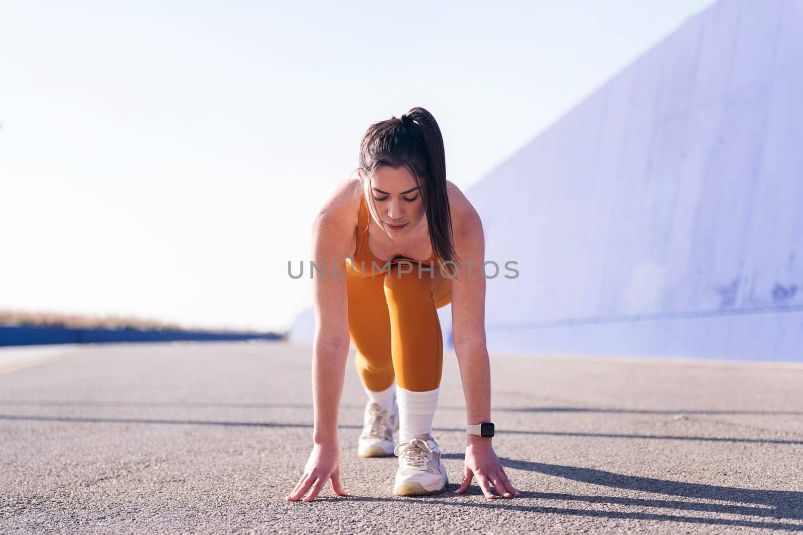 concentrated sportswoman in position to start a race in a sunny day, concept of sport and active lifestyle, copy space for text