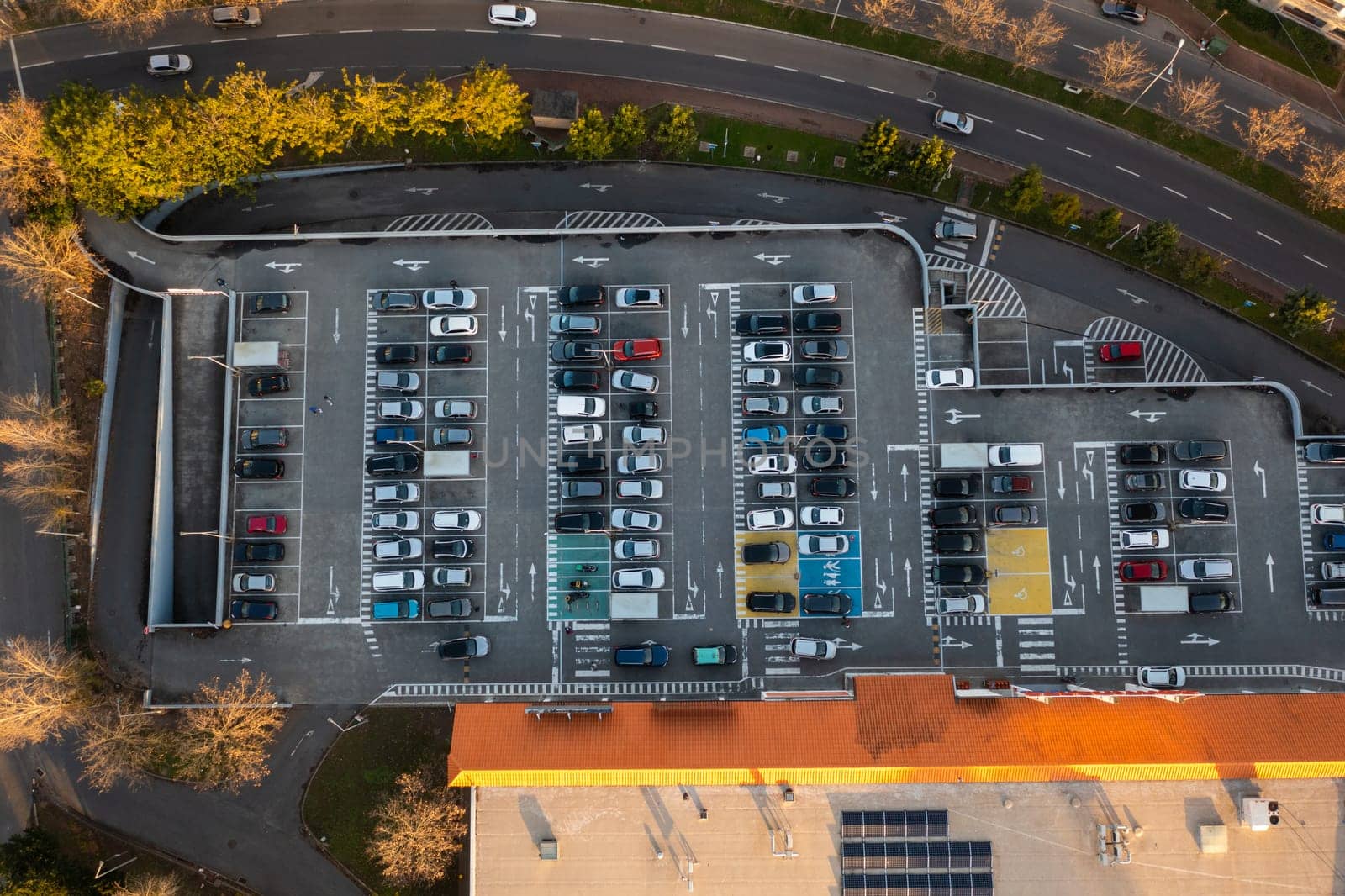 Aerial view of large parking lot in front shopping mall with many parked cars. Carpark at supermarket with lines and markings for vehicle places and directions