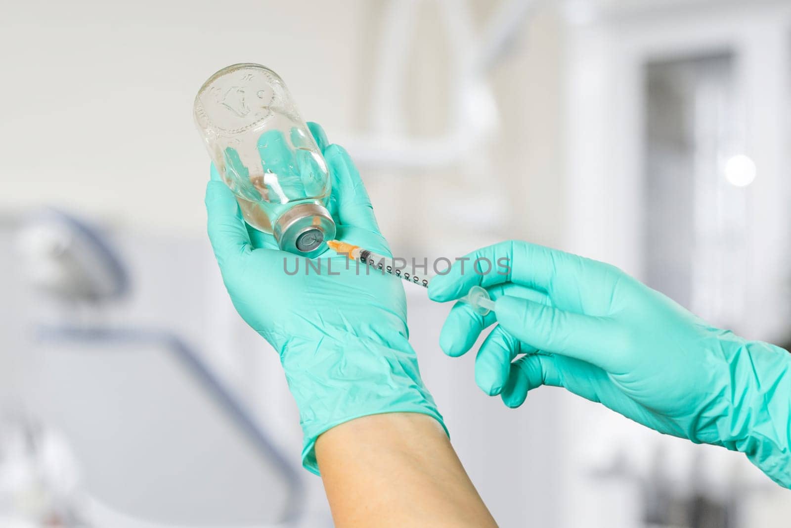 Glass bottle for liquid medicine and a plastic syringe for injection in hands in latex gloves. Dental office on the background.