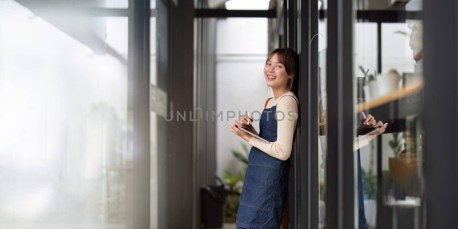 Asian woman barista holding tablet for checking order from customer on blurred coffee cafe shop background , SME business concept.