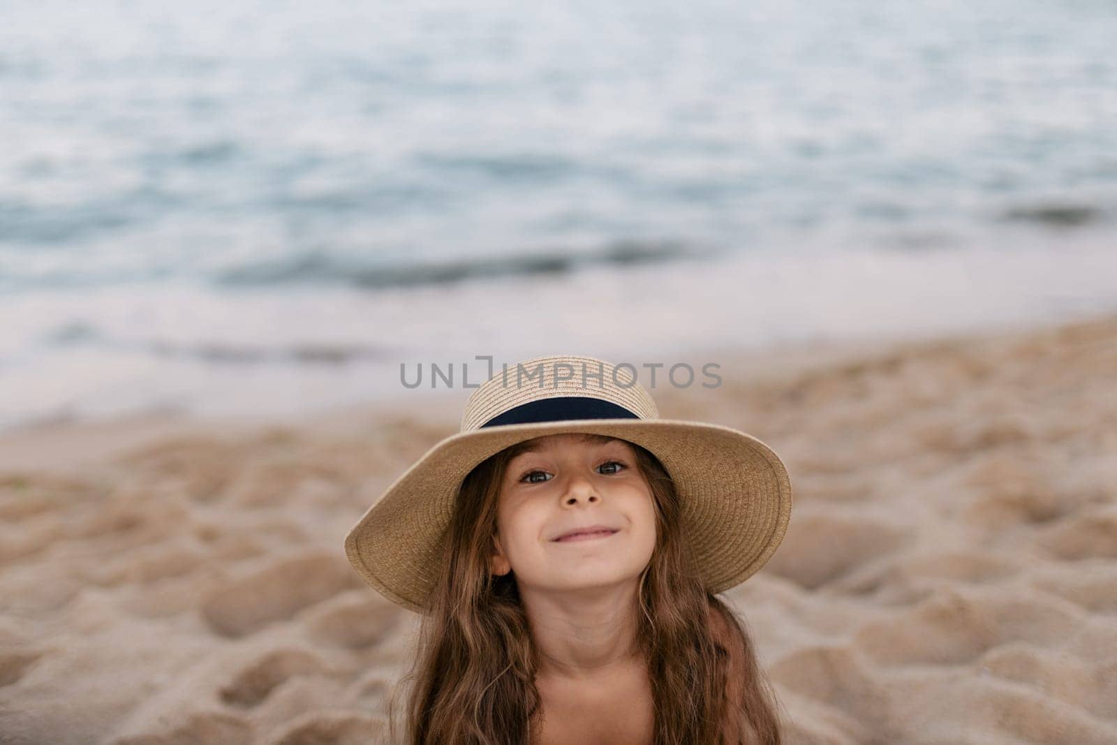a baby girl in her sun hat on the beach.
