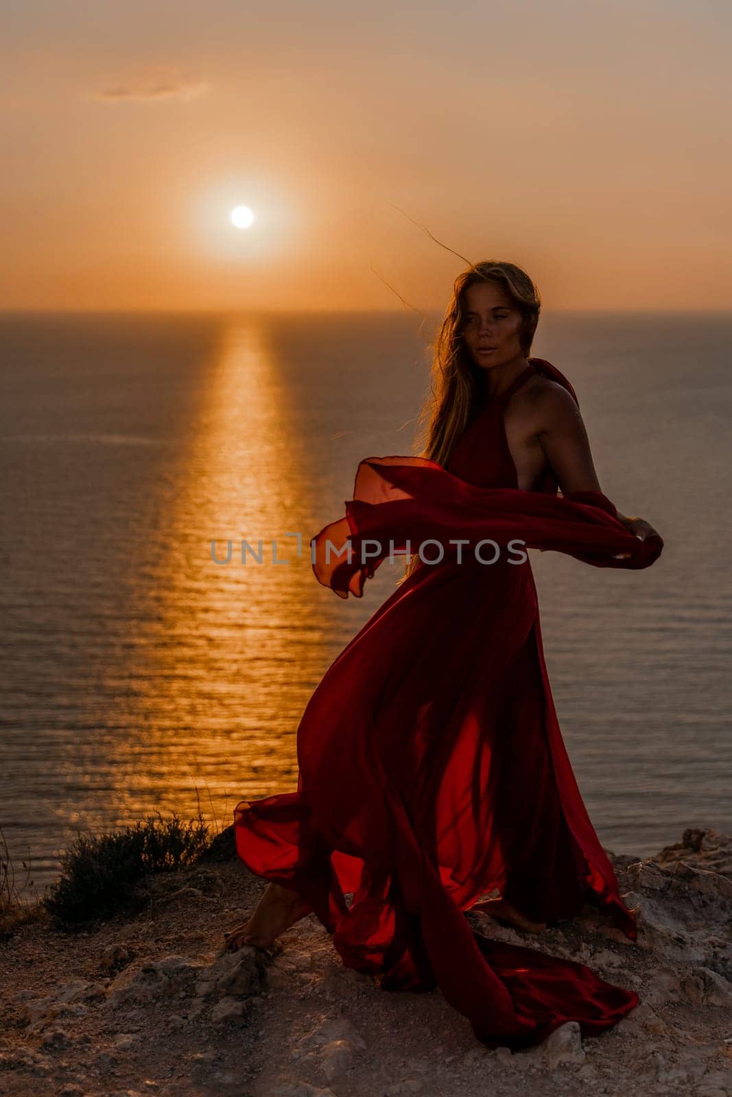 Woman sunset sea red dress, back view a happy beautiful sensual woman in a red long dress posing on a rock high above the sea on sunset