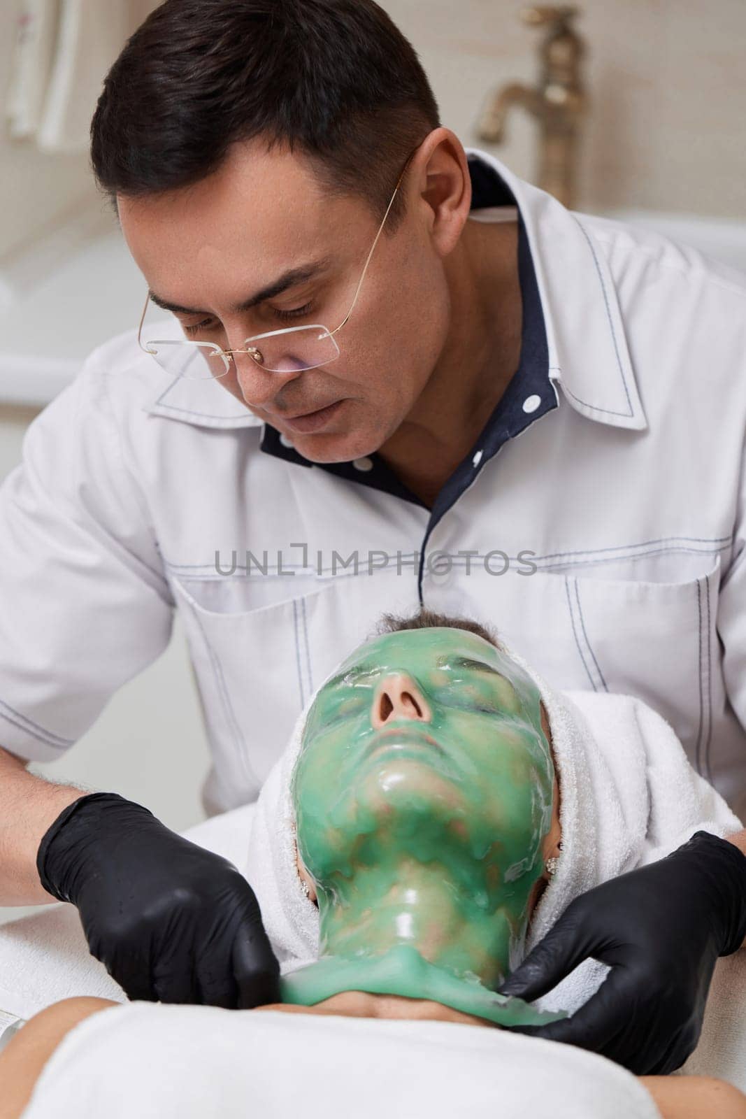 male beautician removing green alginate mask from face of woman by erstudio