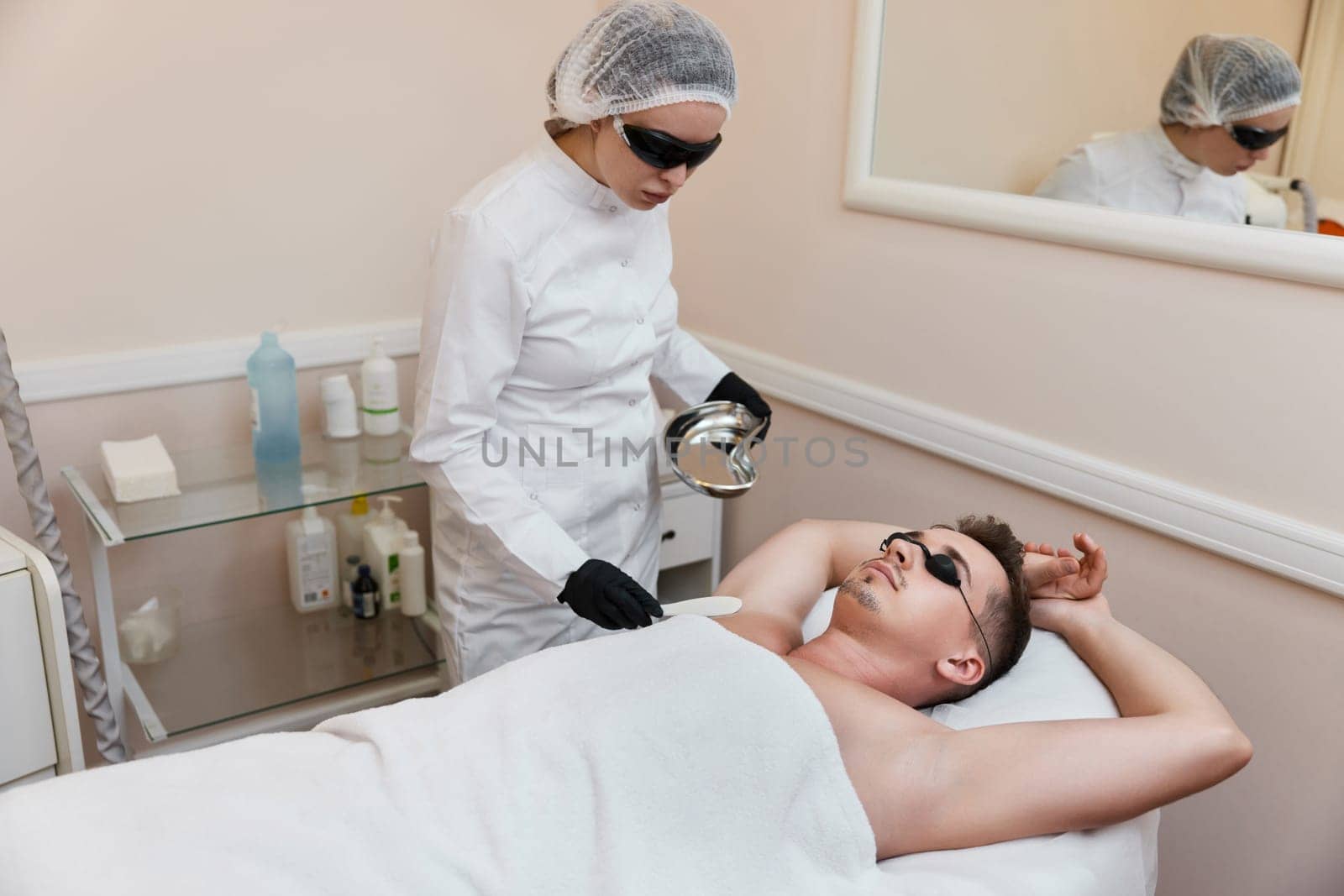 young man with protective goggles undergoes procedure of arm pit laser epilation in clinic