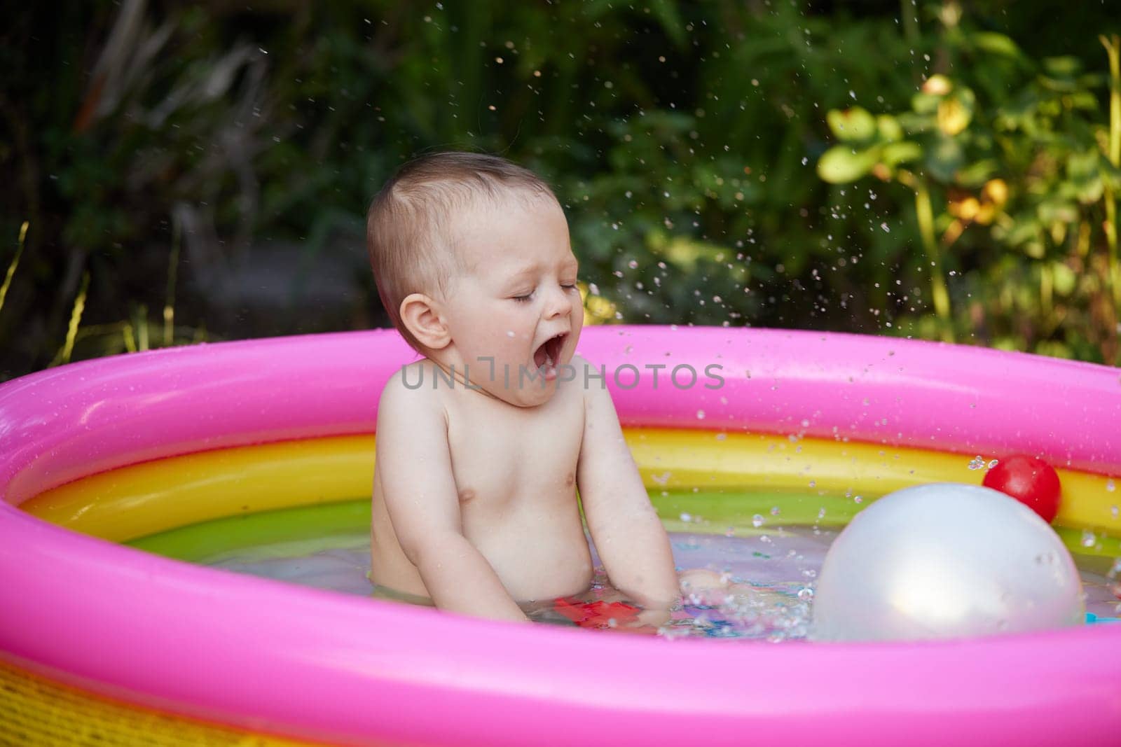 Happy cute baby girl with ball in kid inflatable pool in the garden