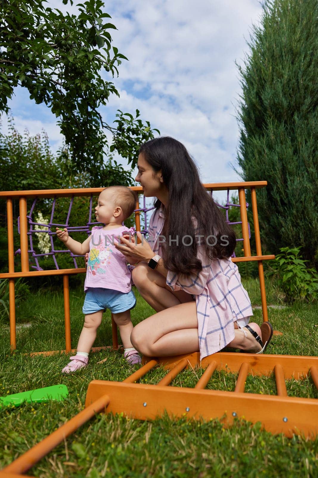 mother with little child girl daughter collects wooden home sports complex outdoor. assembly process