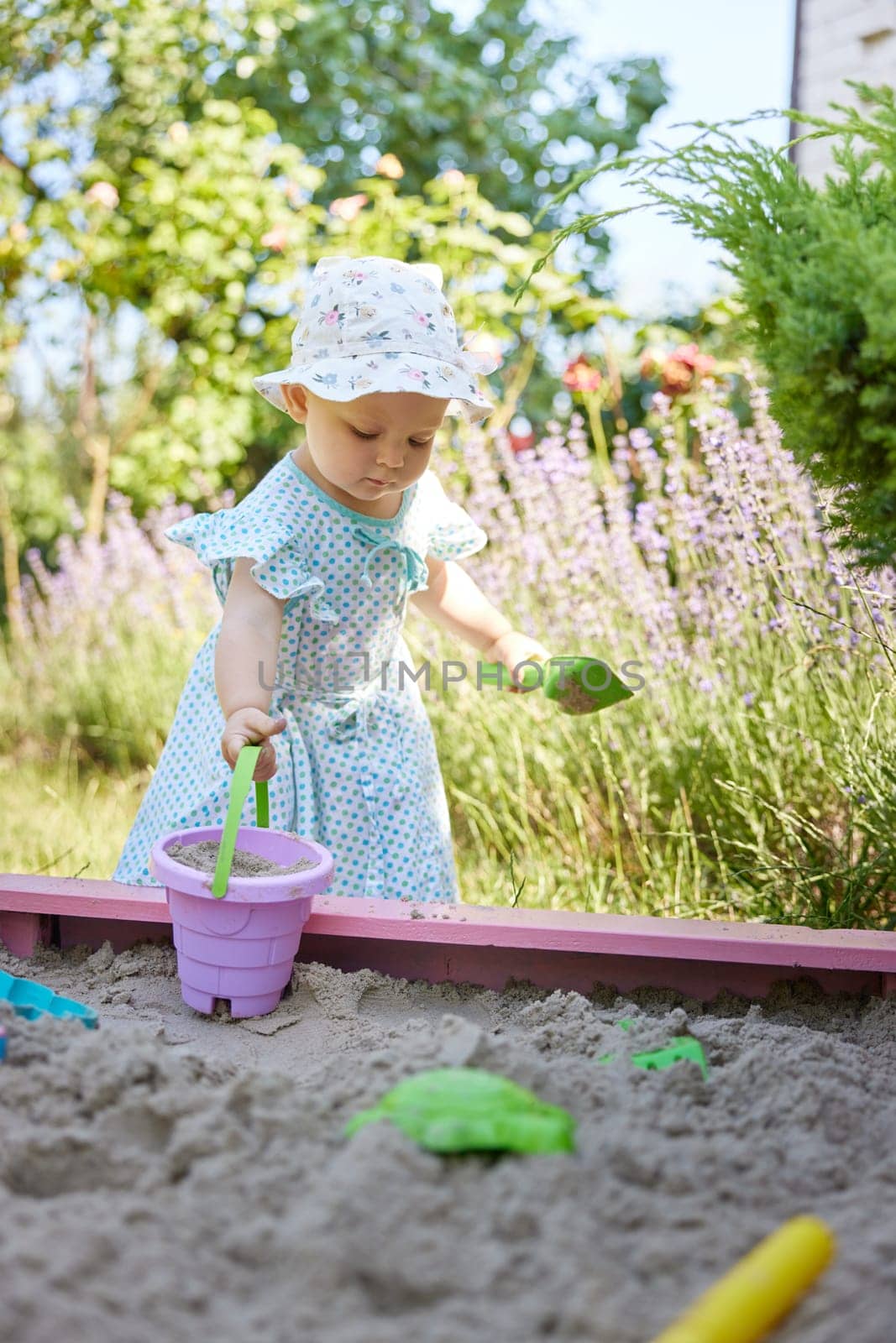 cute little girl playing in sand in sandbox with various toys on outdoor playground
