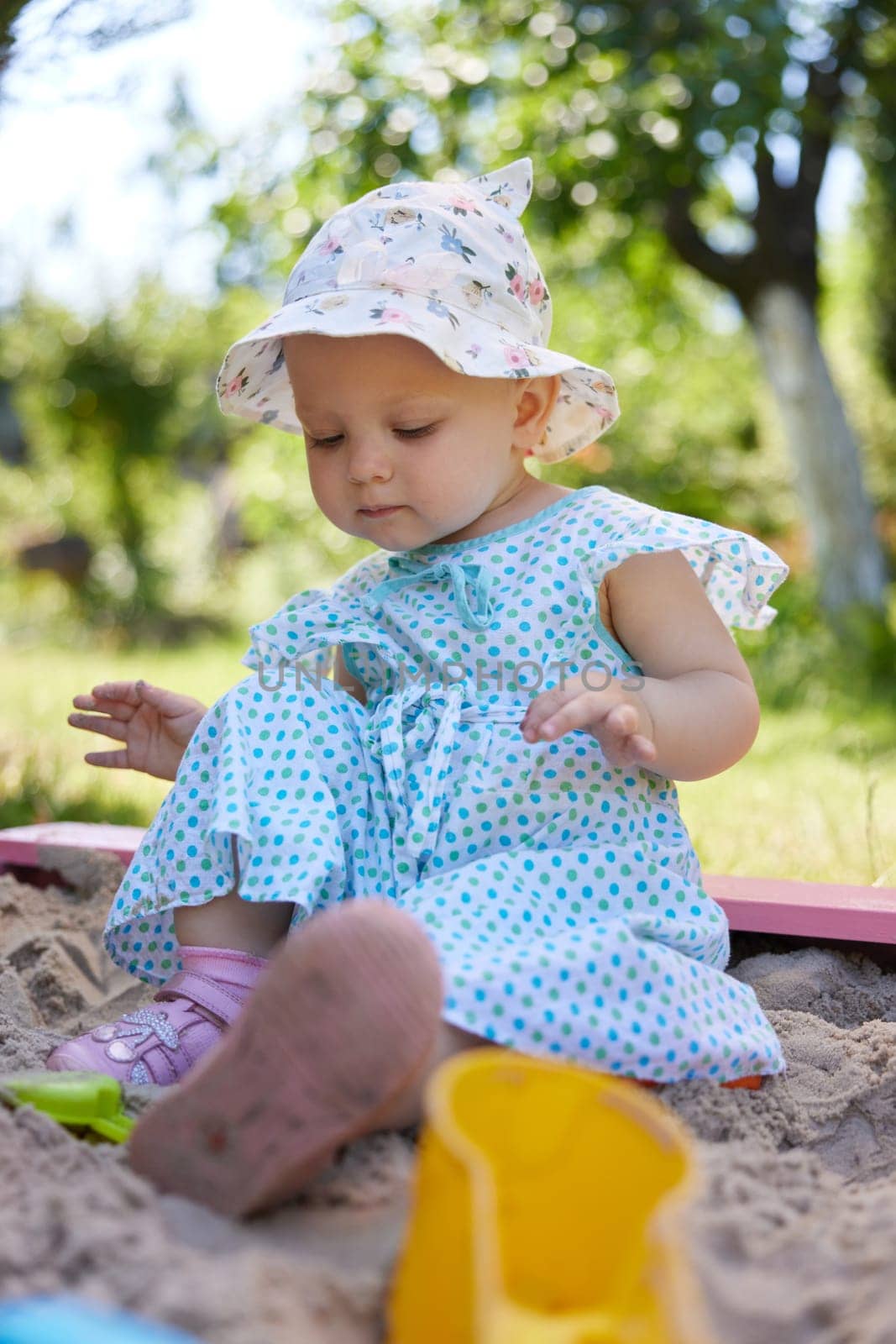 cute little girl playing in sand in sandbox with various toys on outdoor playground on sunny summer day.