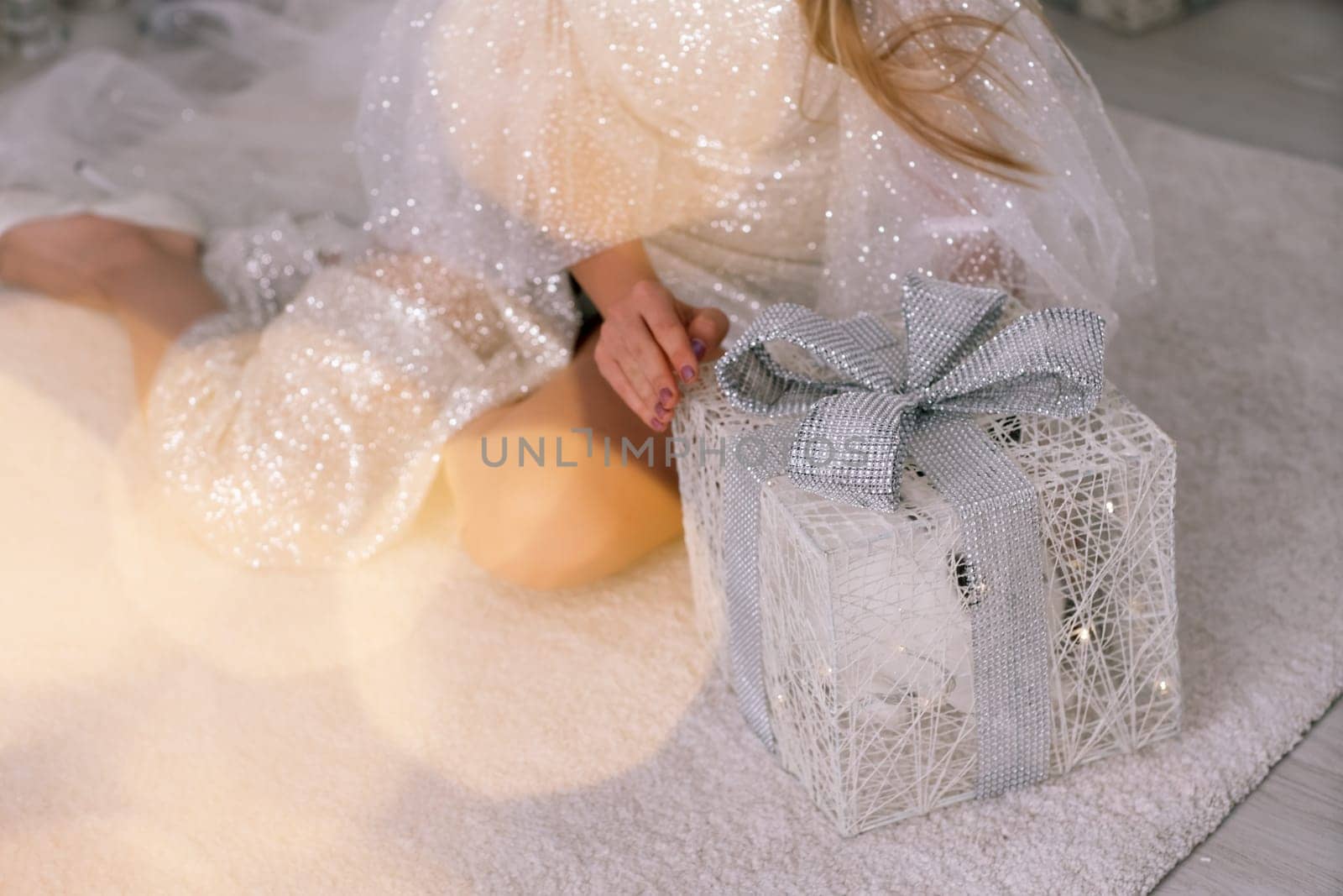 A beautiful box with a gift in the hands of a girl, she sits in a brilliant dress and holds it in her hands. Bokeh from garlands