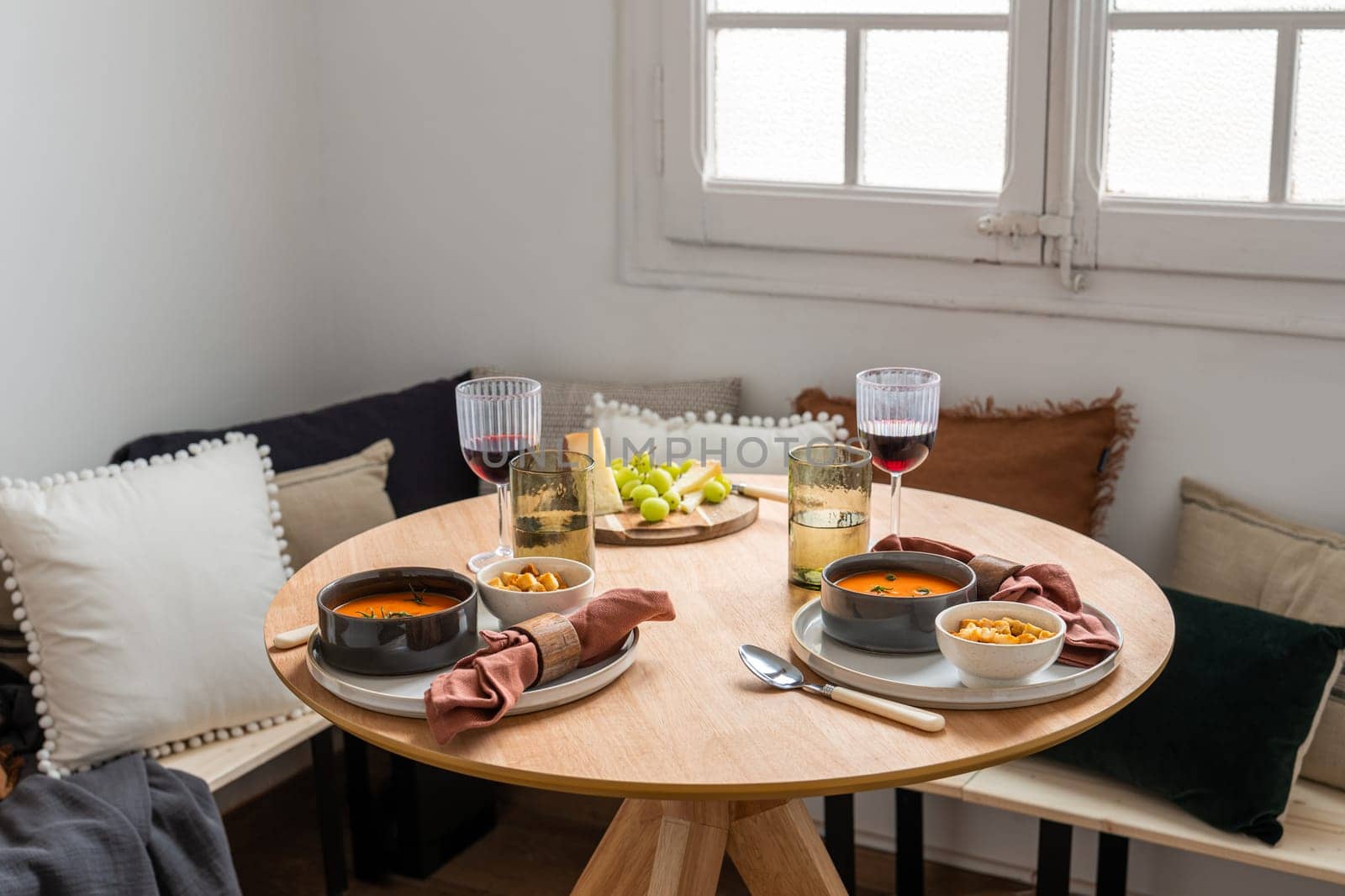 A traditional table is set for a meal in a domestic room. It features food, drink, furniture, and traditional Spanish gazpacho.