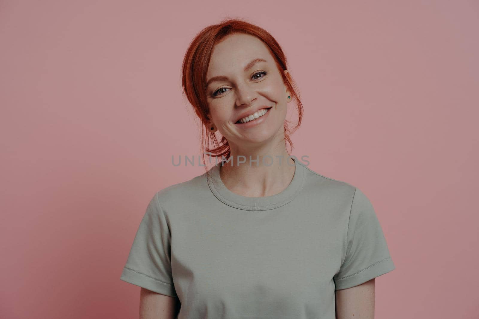 Happy people concept. Positive relaxed redhead woman with pleasant appearance smiling cheerfully, carefree red-haired female dressed in casual outfit relaxing indoors, isolated on pink background