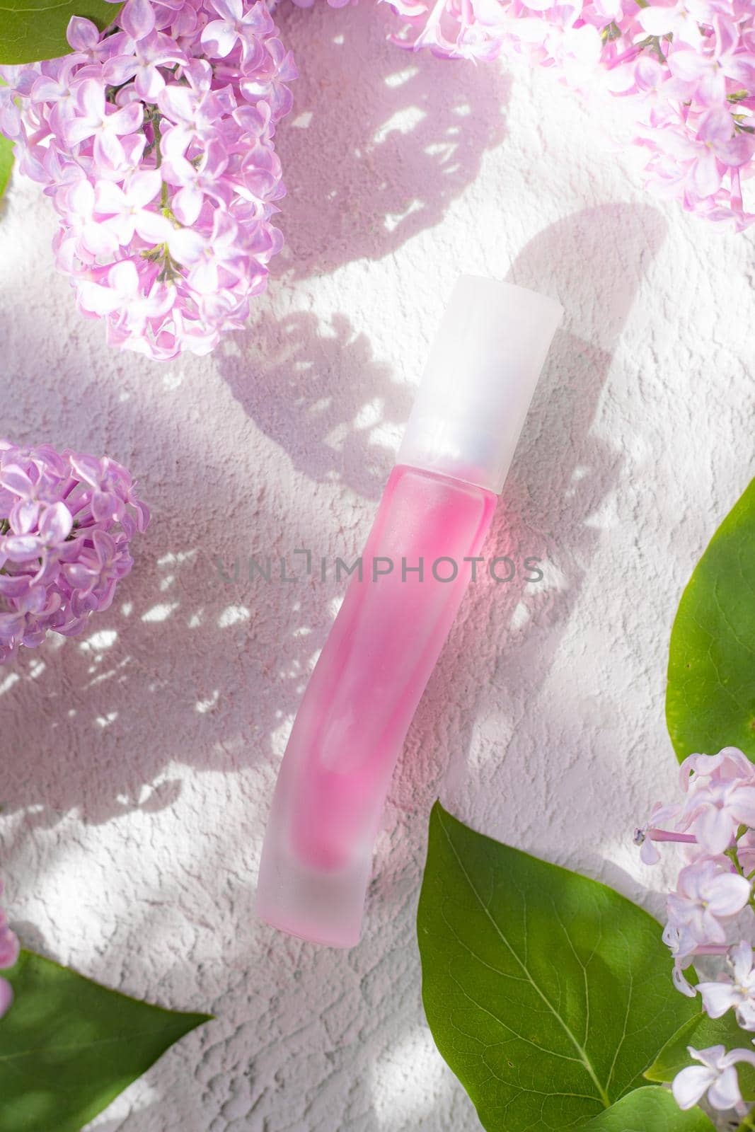 Pink perfume bottle and lilac branch light and shade. The concept of advertising perfumes. A bottle of perfume without text. Floral aromatherapy layout . Copy space