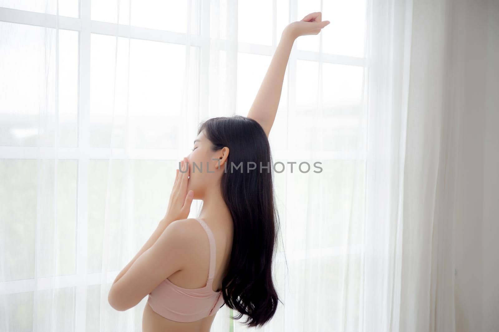 Beautiful young asian woman waking up in the morning stand stretching arms and yawn in the bedroom, sexy girl in underwear relax cozy and wake with fresh happy at home, lifestyle concept, back view.