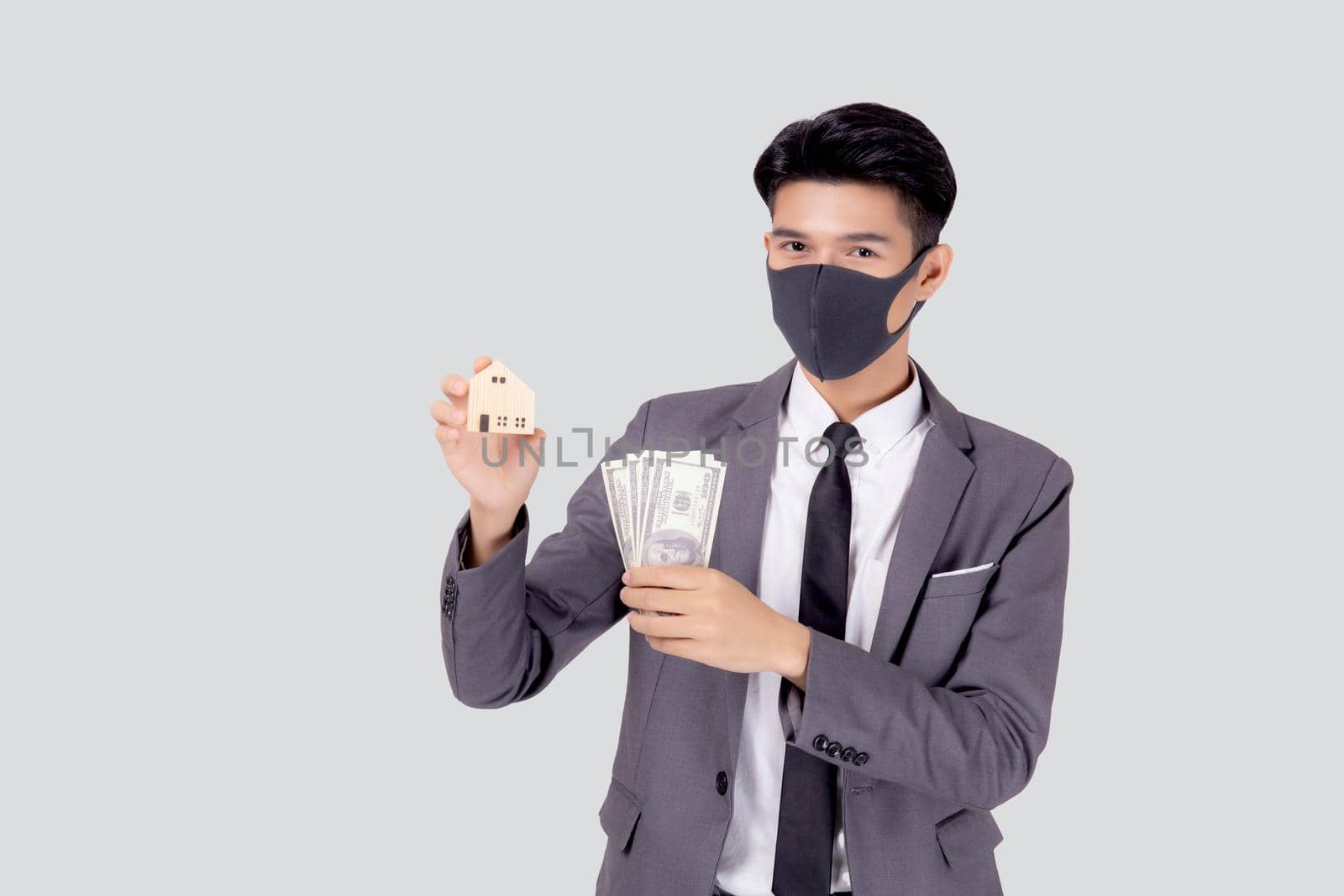 Young asian businessman in face mask holding money dollar and home isolated on white background, pandemic and crisis of economic, business man and investment property during disease covid-19. by nnudoo