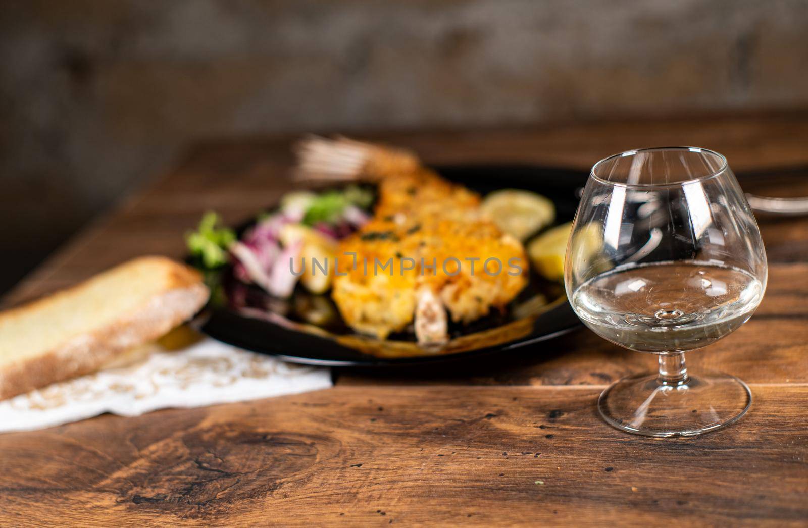 monkfish au gratin plate with composition on wooden top and wine glass and cutlery