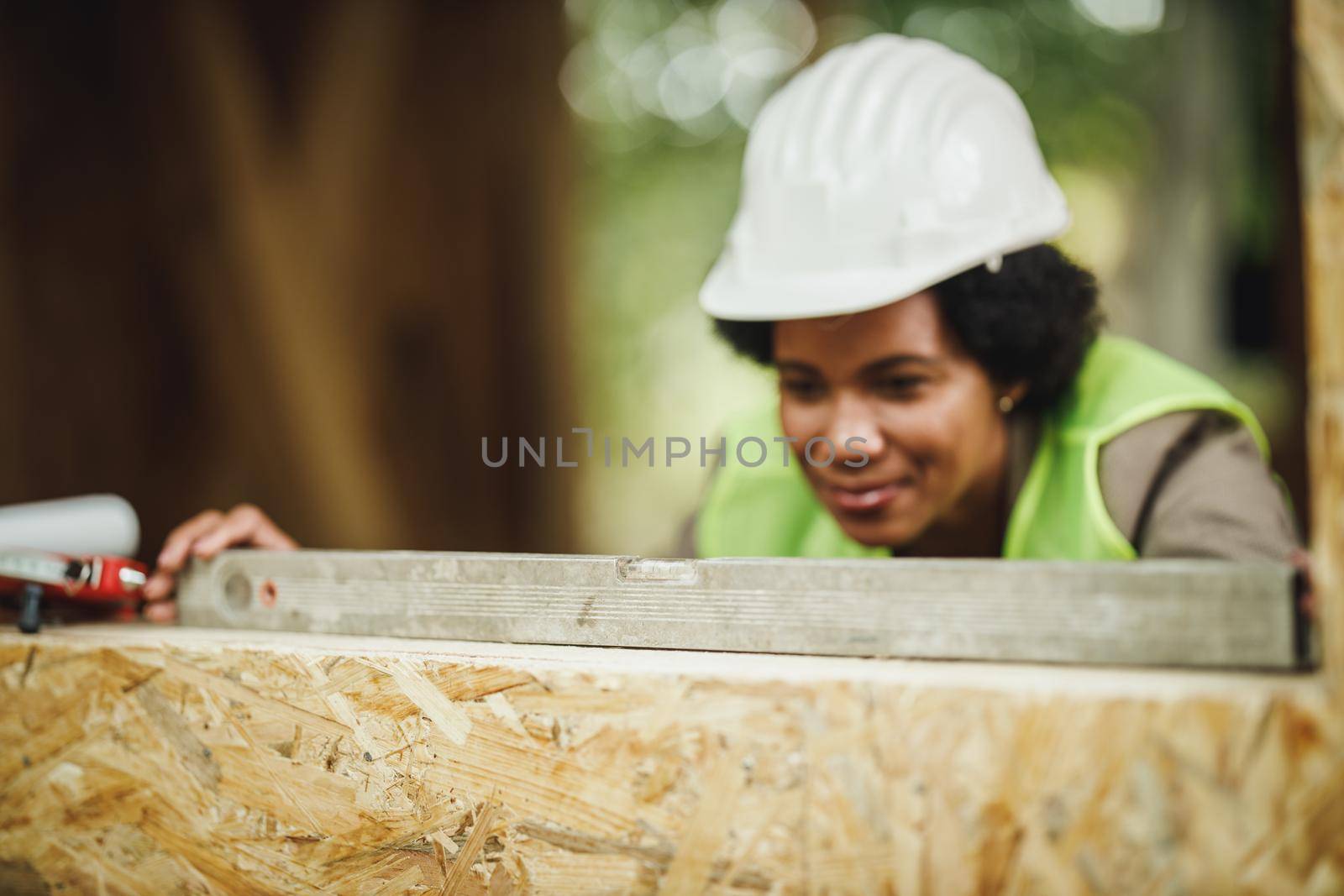 Shot of an African female architect using level on window to check new wood house.