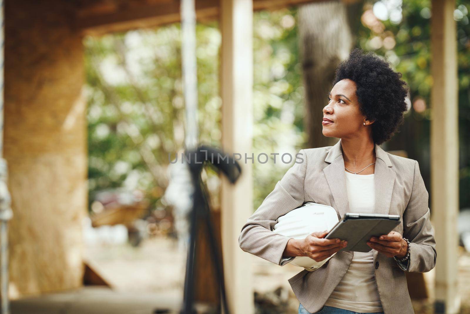 Shot of an African female architect using a digital tablet and checking construction site of a new wooden house.