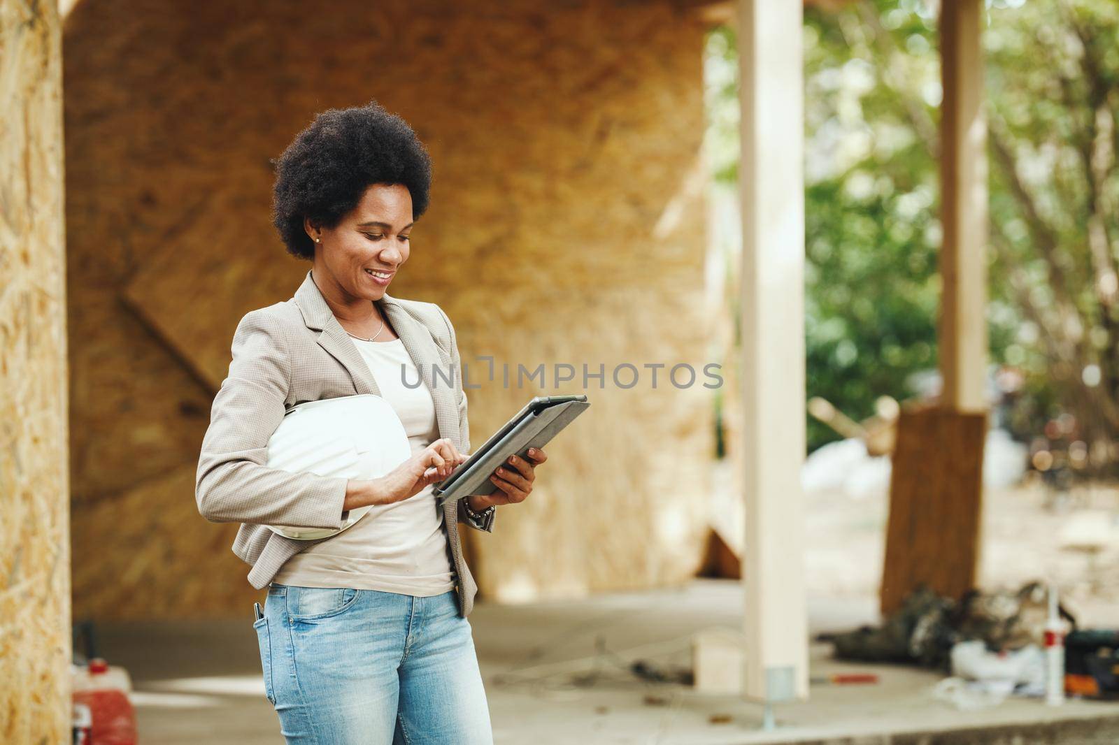 Shot of an African female architect using a digital tablet and checking construction site of a new wooden house.